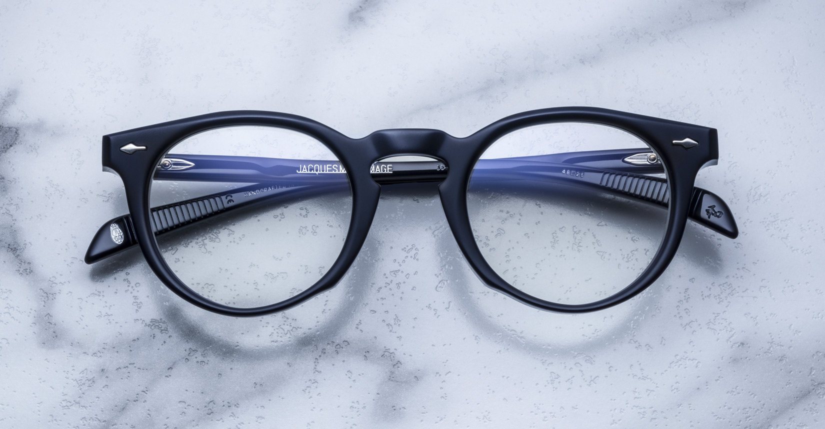 Jacques Marie Mage Percier black eyeglasses with blue arms, top-down view.
