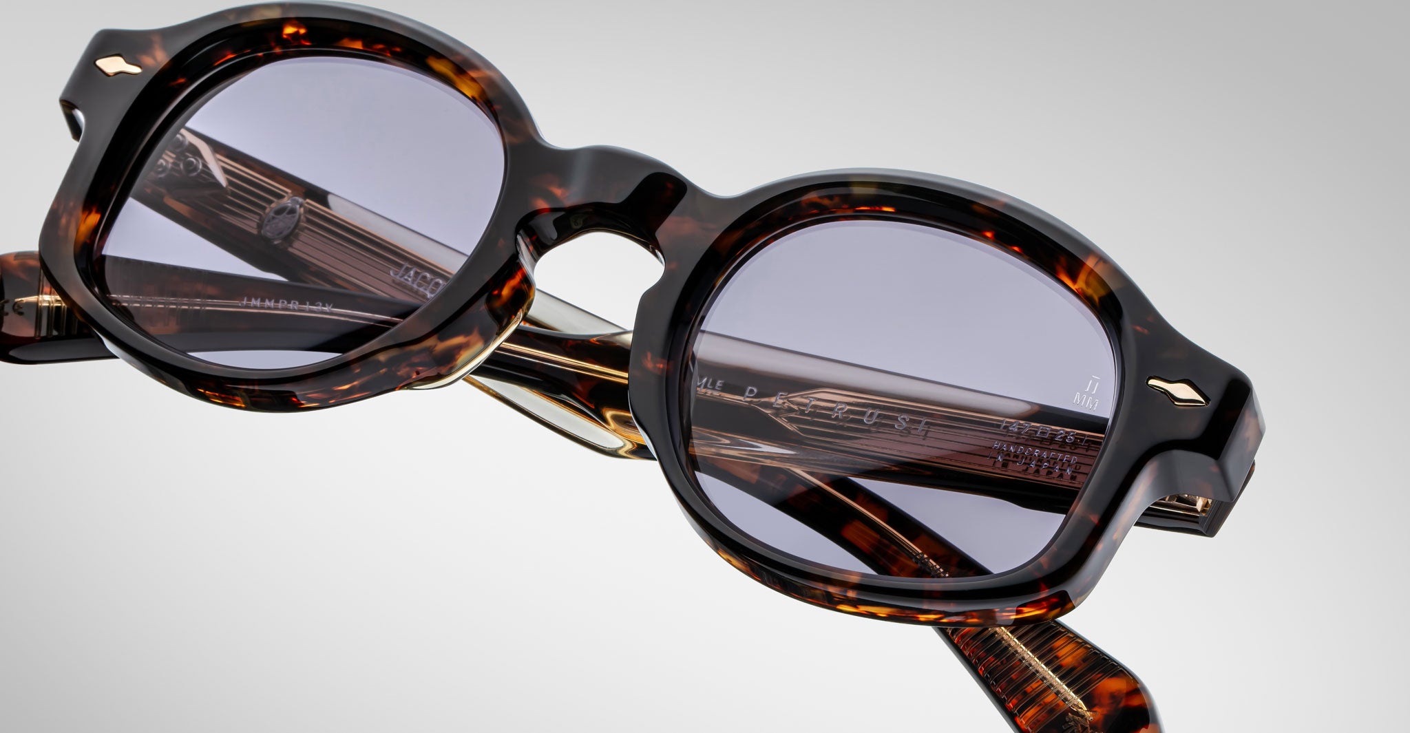 A close-up of Jacques Marie Mage Petrus tortoiseshell round eyeglasses with dark lenses displayed on a white surface, highlighting the detailed thick frames and temples with visible engraved markings.