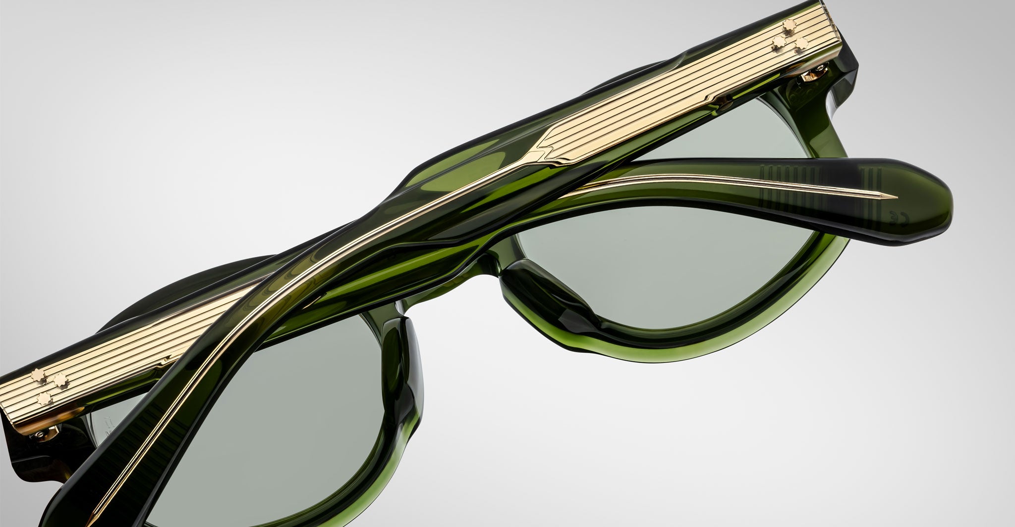 A close-up view of Jacques Marie Mage Petrus sunglasses in green with gold metal temple accents, folded and set against a plain light gray background.