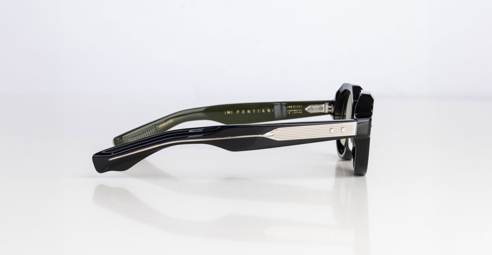 The Jacques Marie Mage Pontian eyeglasses are displayed from the side on a white surface, emphasizing their thick black arms with metallic and textured accents, and the brand name visible on the inner left temple.