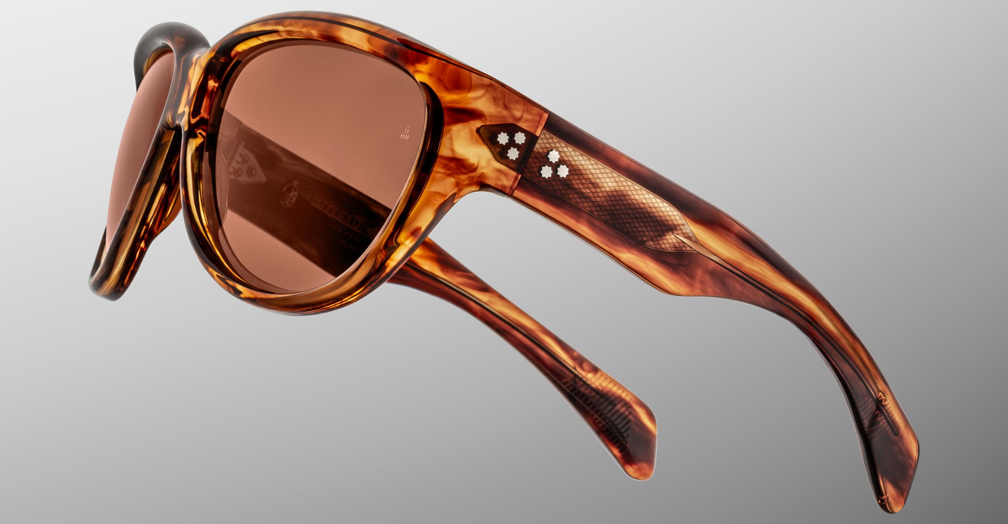 Close-up of Jacques Marie Mage Ravello tortoiseshell sunglasses with brown tinted lenses, showcasing a textured design and distinctive white dot details on the arms, set against a neutral gray background.
