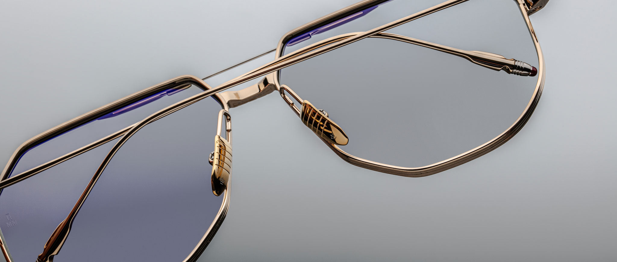 Close-up of Jacques Marie Mage Reynold eyeglasses, gold frame with blue-tinted lenses, minimalist style, front angle view.