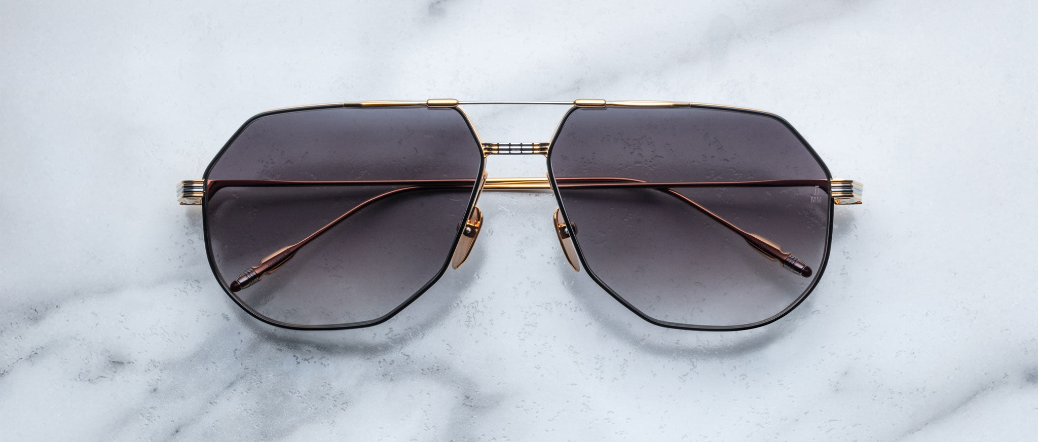Jacques Marie Mage Reynold aviator sunglasses with dark lenses and gold frames, shown from above on white marble.
