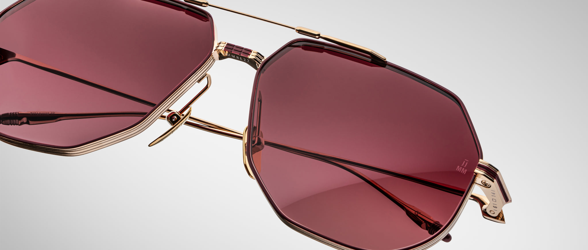 Close-up of Jacques Marie Mage Reynold sunglasses featuring geometric rose-tinted lenses and gold frames, viewed from the front.