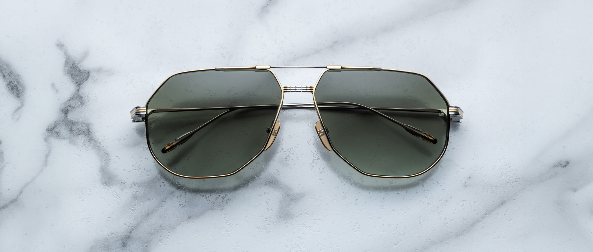 Jacques Marie Mage Reynold aviator sunglasses with gold frames and dark lenses, top-down view.