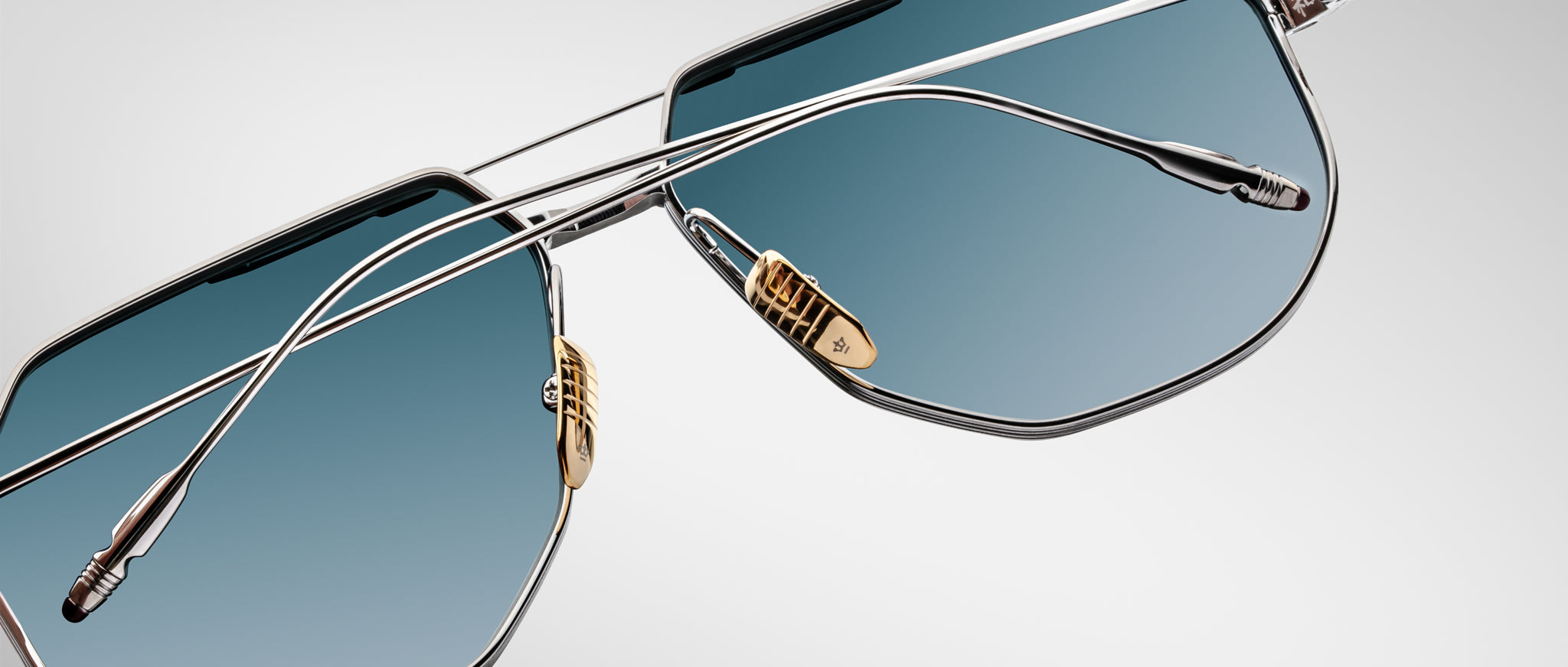 Close-up of Jacques Marie Mage Reynold sunglasses showing blue lenses, silver metal frame, and gold nose pads.