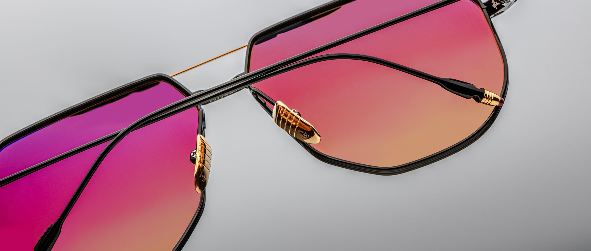 Close-up of Jacques Marie Mage Reynold sunglasses showing black frames and pink-orange gradient lenses, viewed from the front.