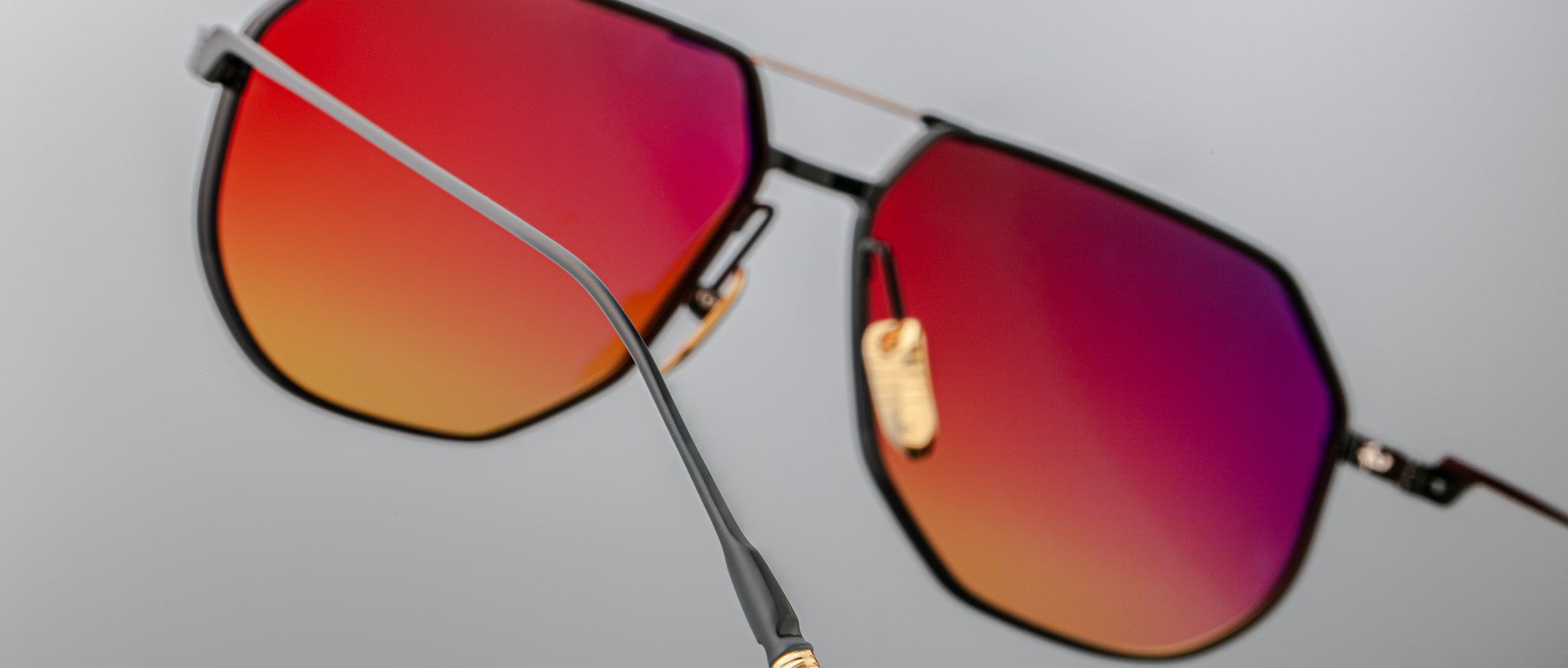 Close-up of Jacques Marie Mage Reynold sunglasses, black frames, red-orange lenses, product shown from the front angle.