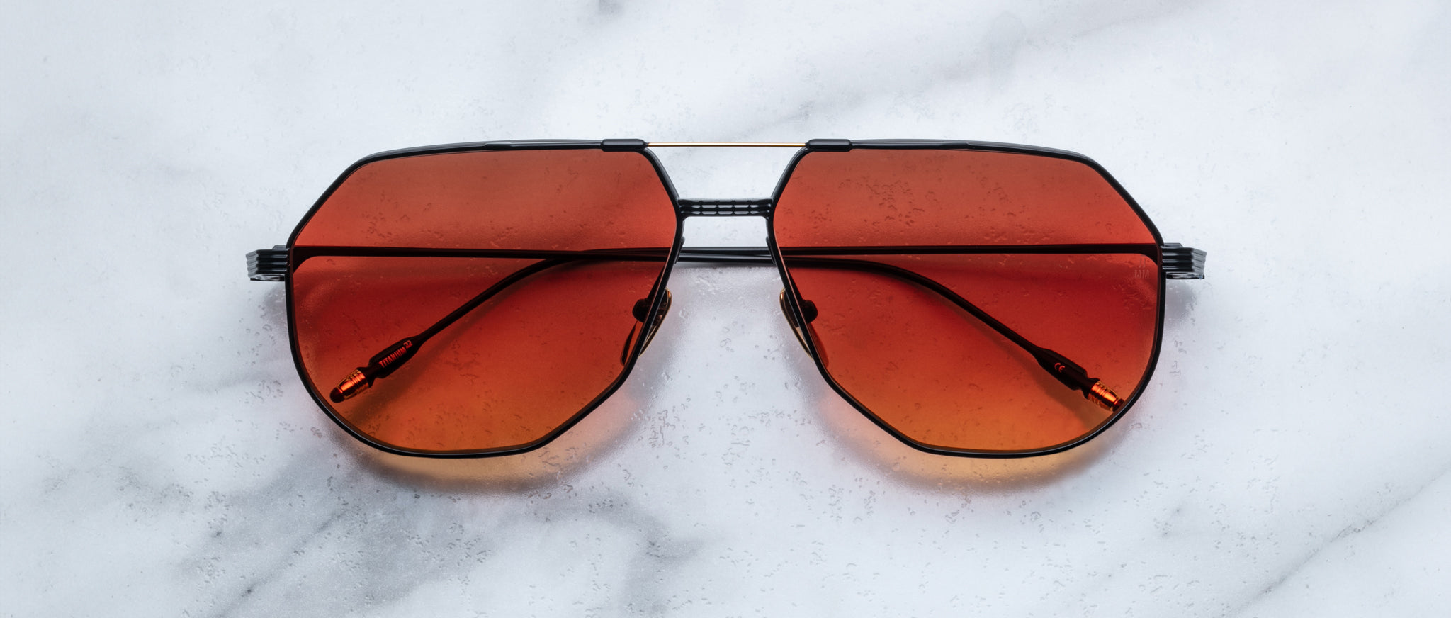 Jacques Marie Mage Reynold sunglasses feature orange lenses and black frames, shown from above.