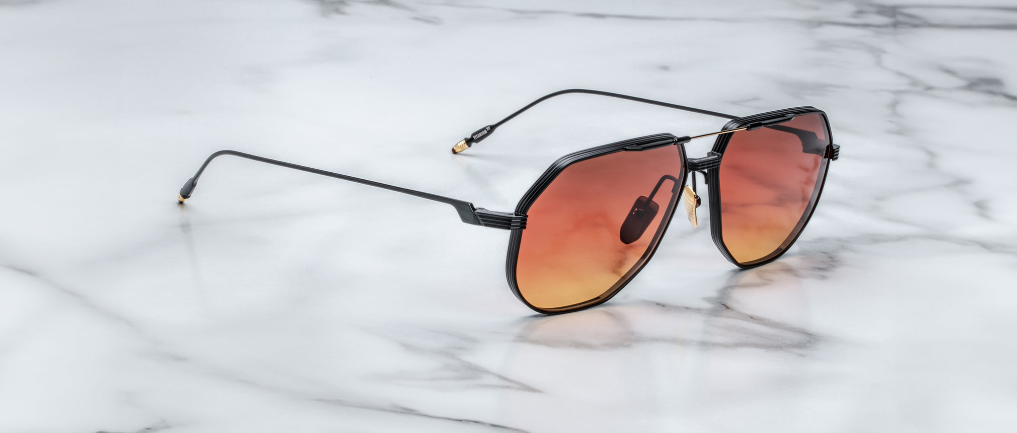 Jacques Marie Mage Reynold sunglasses, thin black frames, red-orange gradient lenses, viewed from above.