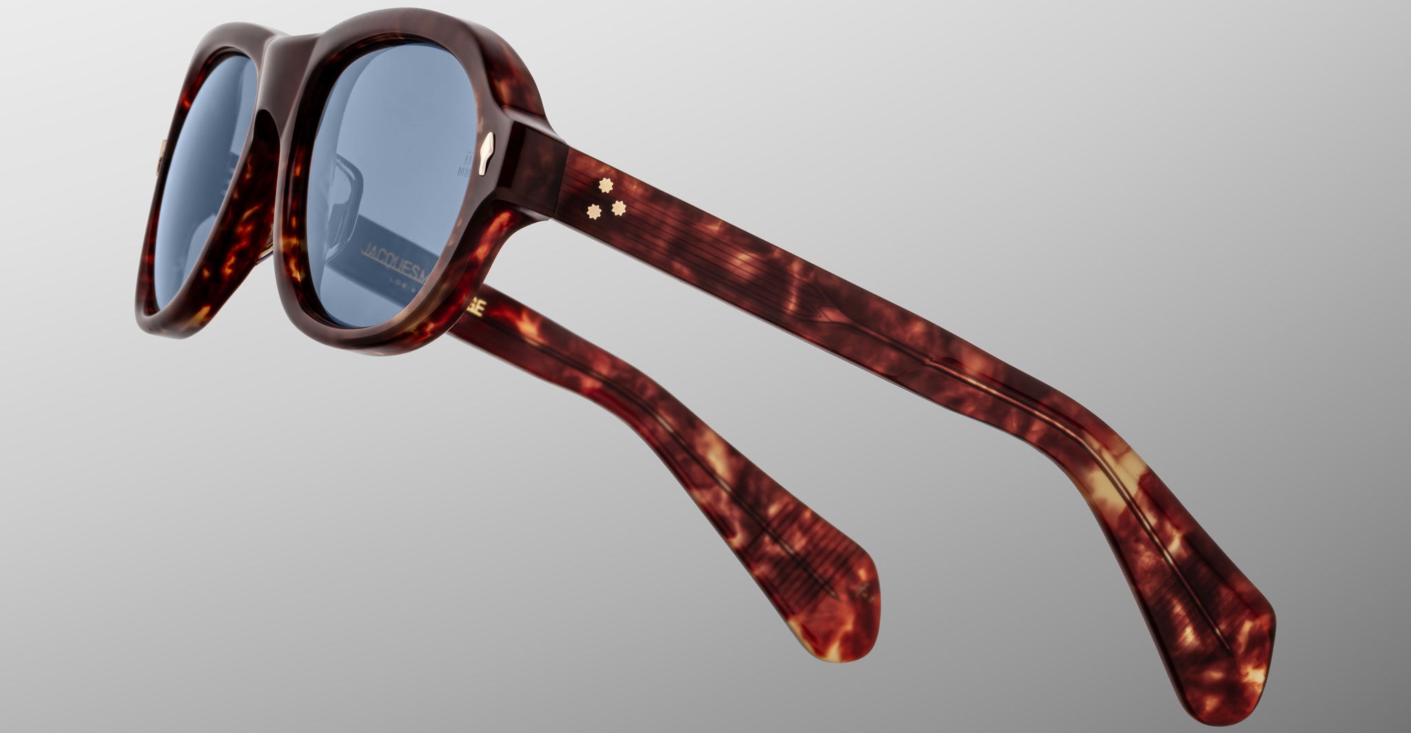 Close-up of Jacques Marie Mage Richard sunglasses featuring tortoiseshell-patterned thick frames and dark lenses, displayed against a light grey background. The brand name appears on the inner arm.