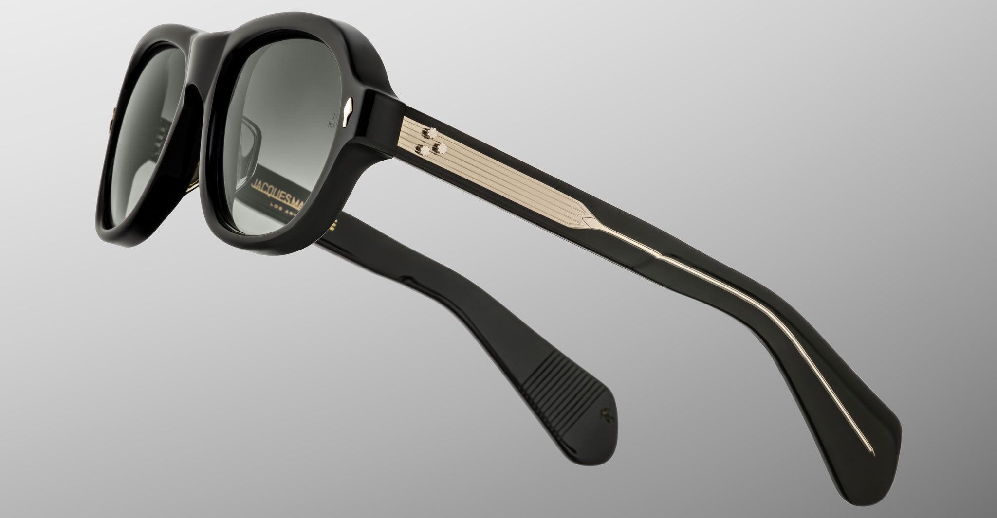 Jacques Marie Mage Richard sunglasses feature thick black frames, dark lenses, and gold accents on the arms, showcased against a light gray background.