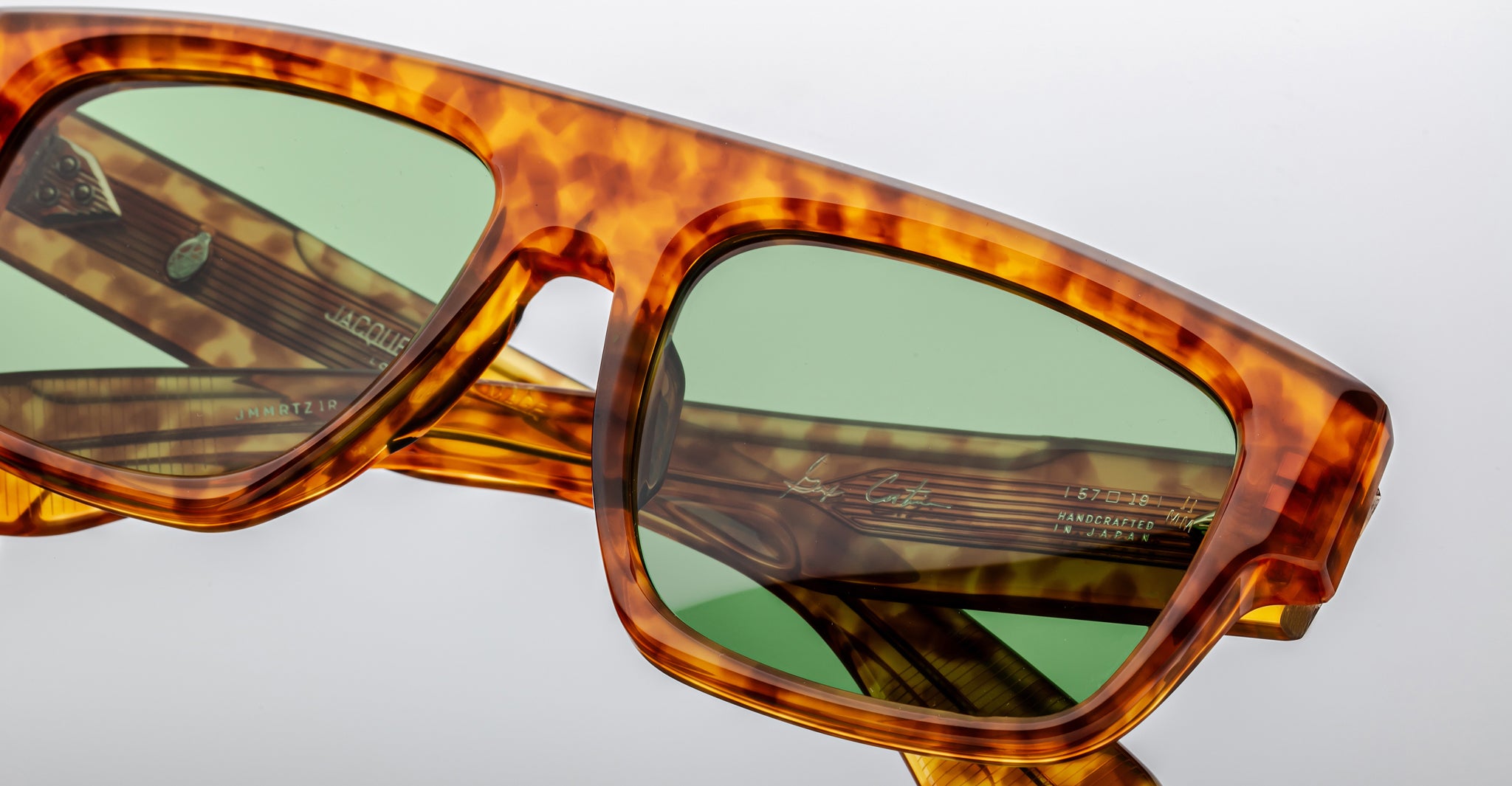Close-up of Jacques Marie Mage Ritz tortoiseshell rectangular sunglasses with green-tinted lenses, highlighting detailed frame texture and partially visible branding or model info on the inner arms.