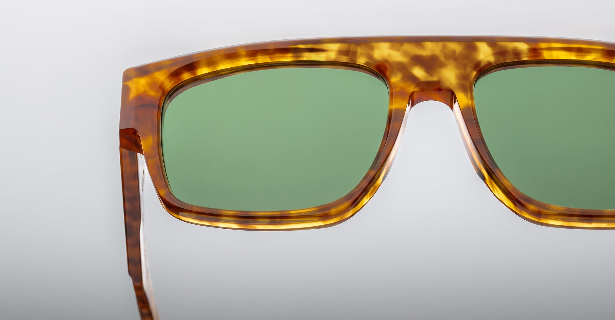 Close-up of the upper half of Jacques Marie Mage Ritz sunglasses featuring green lenses and a thick, mottled brown tortoiseshell frame against a plain light background.