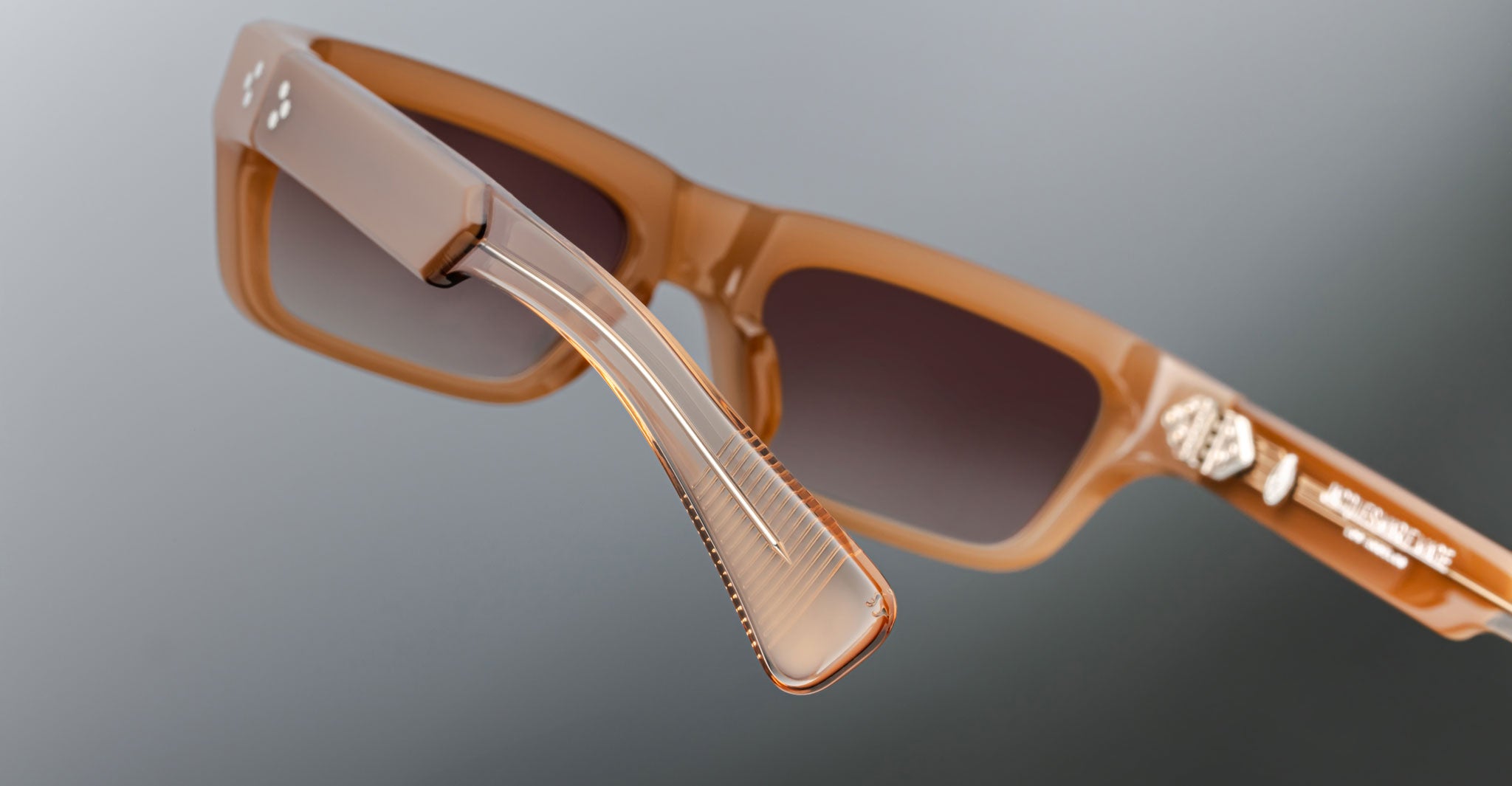 Close-up view of Jacques Marie Mage Rush brown rectangular sunglasses with brown-tinted lenses, highlighting the hinge and arm details. The arm shows horizontal ridges and logo text near the hinge.