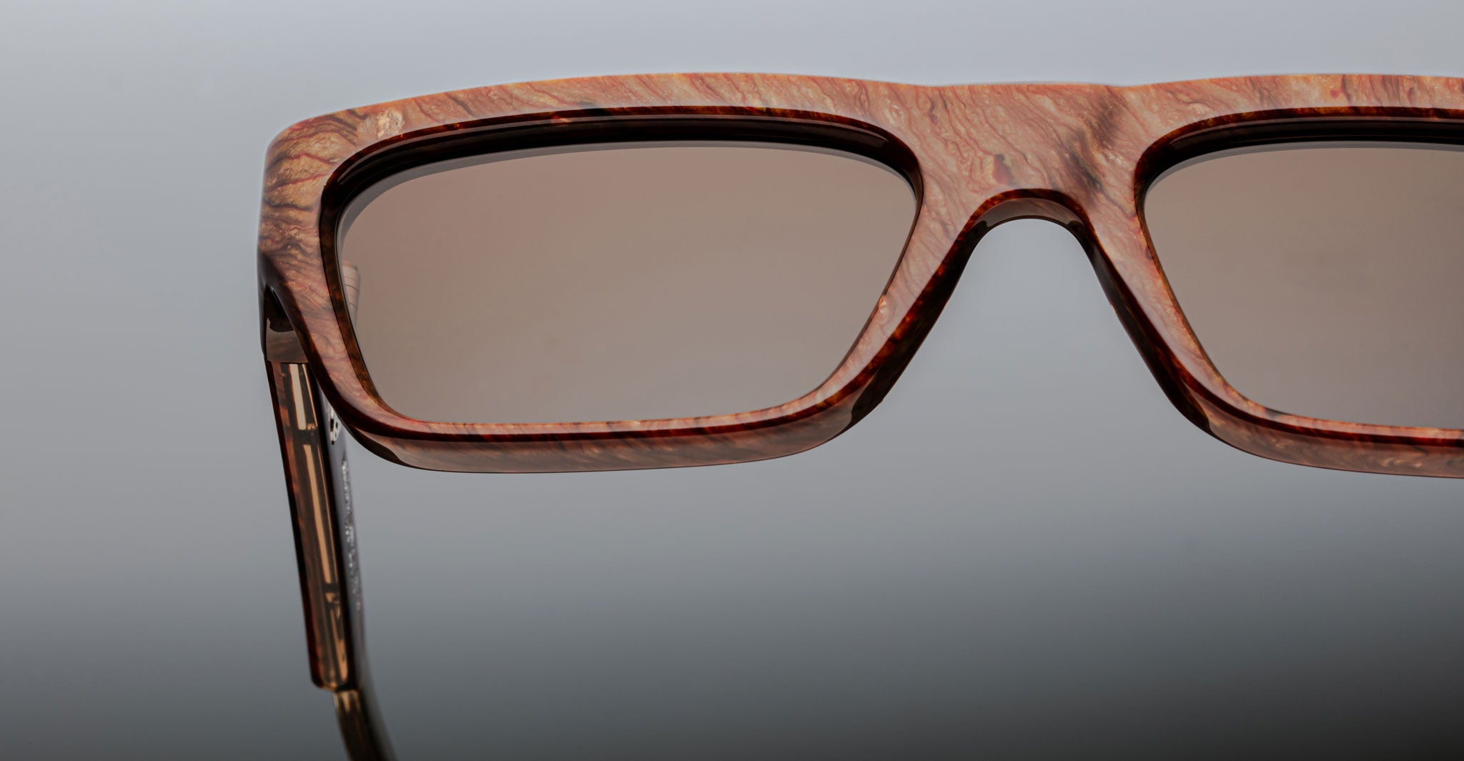 Close-up of the left side of Jacques Marie Mage Rush rectangular sunglasses with wood-textured frames and brown-tinted lenses, set against a neutral background.