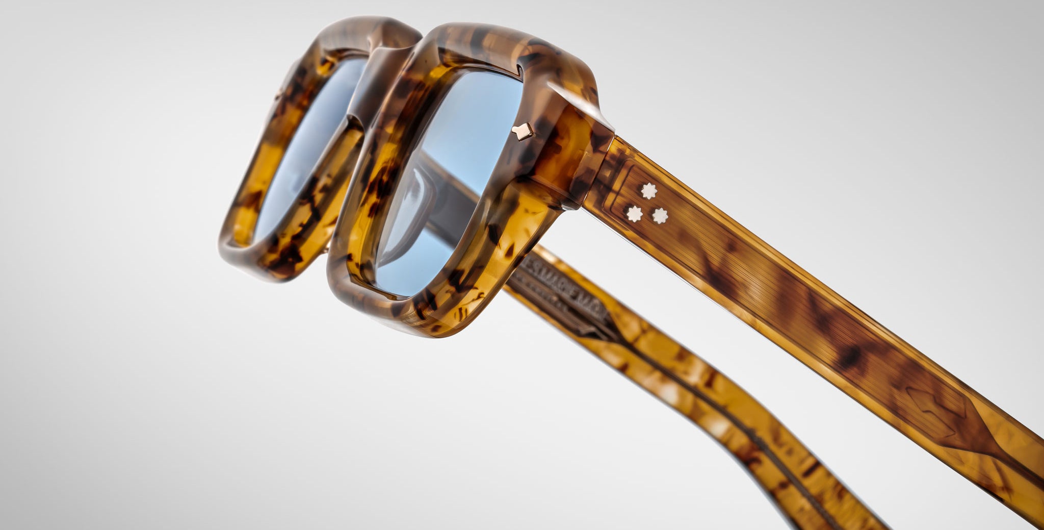 Close-up view of Jacques Marie Mage Sandro square eyeglasses in a tortoiseshell pattern, featuring blue-tinted lenses and two small star-shaped metal accents on the temples, shown against a plain background.