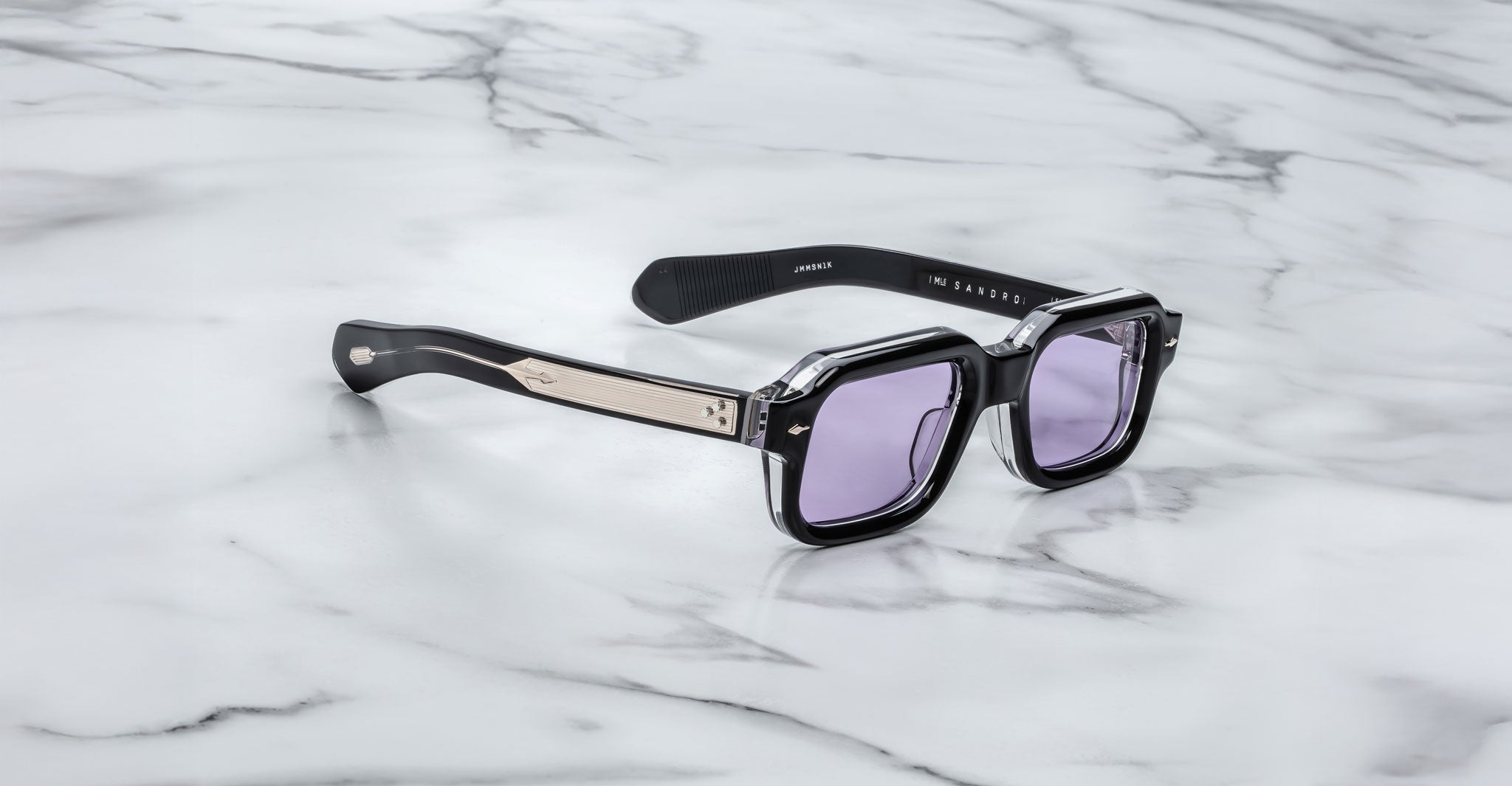 The Jacques Marie Mage Sandro sunglasses feature a black rectangular frame, light purple lenses, and metallic temple detailing, showcased on a white marble surface.