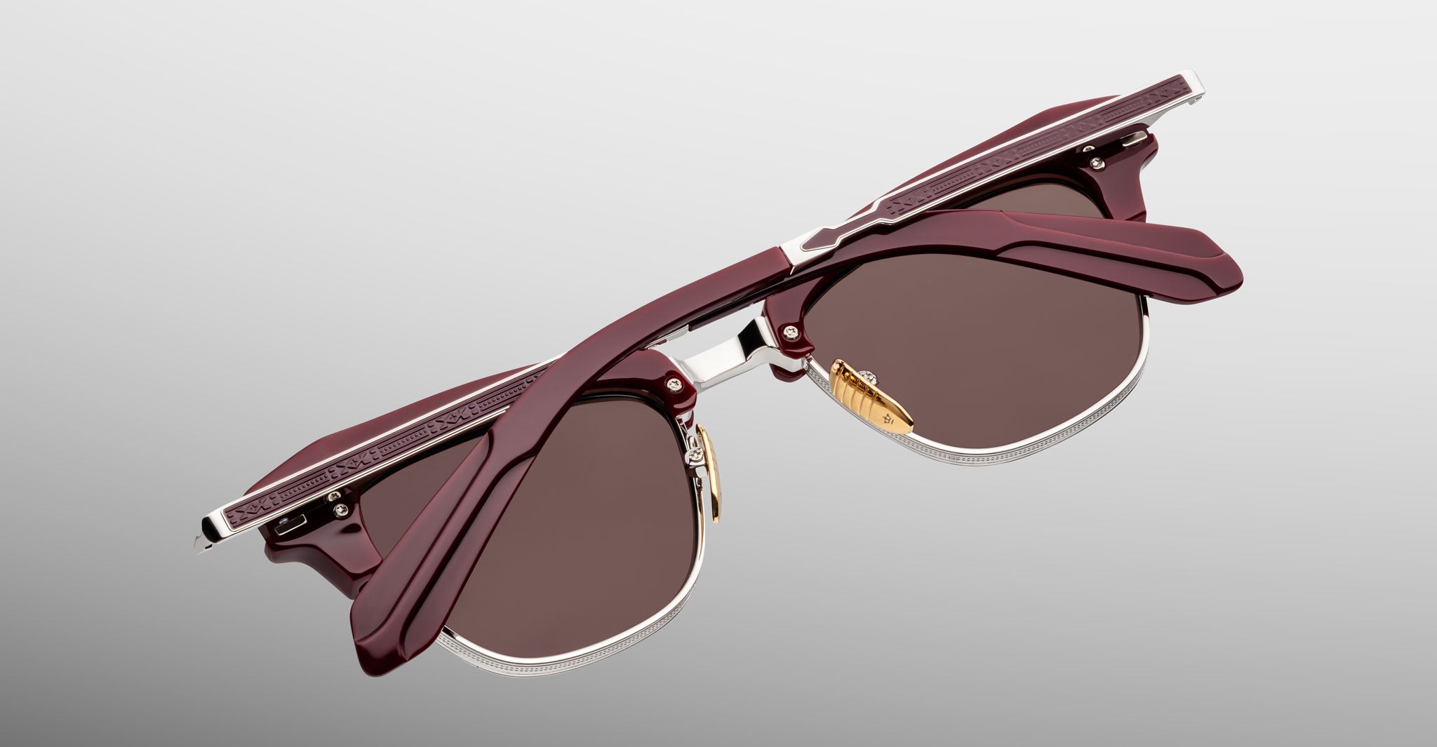 The Jacques Marie Mage Sartre by Jacques Marie Mage: dark red clubmaster optical frames with brown lenses, folded and seen from above on a light gradient background.