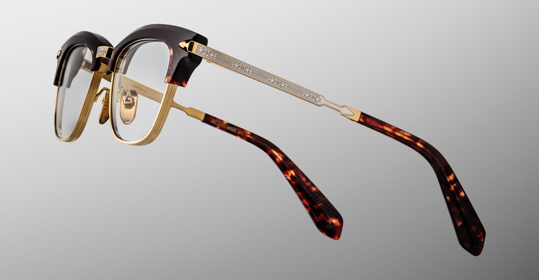 The Jacques Marie Mage Sartre glasses feature gold metal frames, a tortoiseshell-patterned browline and temple tips, and clear nose pads, displayed against a neutral background.