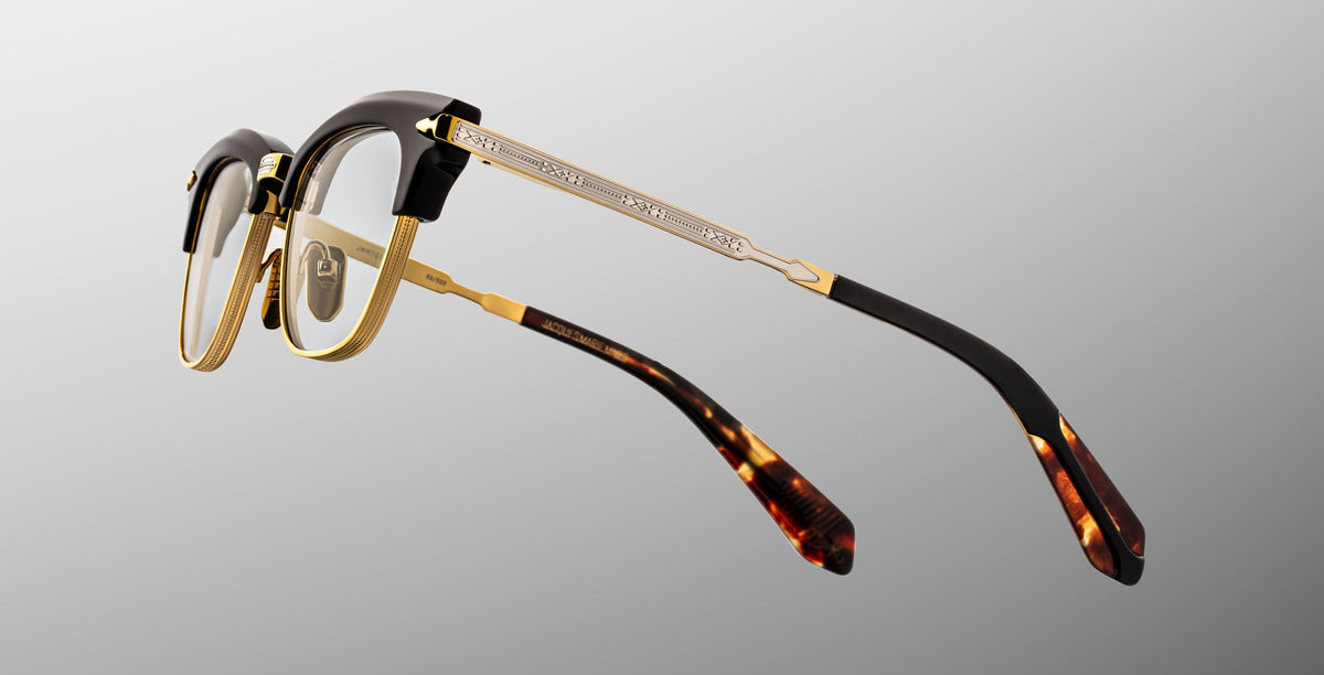 The Jacques Marie Mage Sartre glasses feature gold metal frames, black accents on the browline and temples, and tortoiseshell-patterned temple tips, shown against a neutral background.