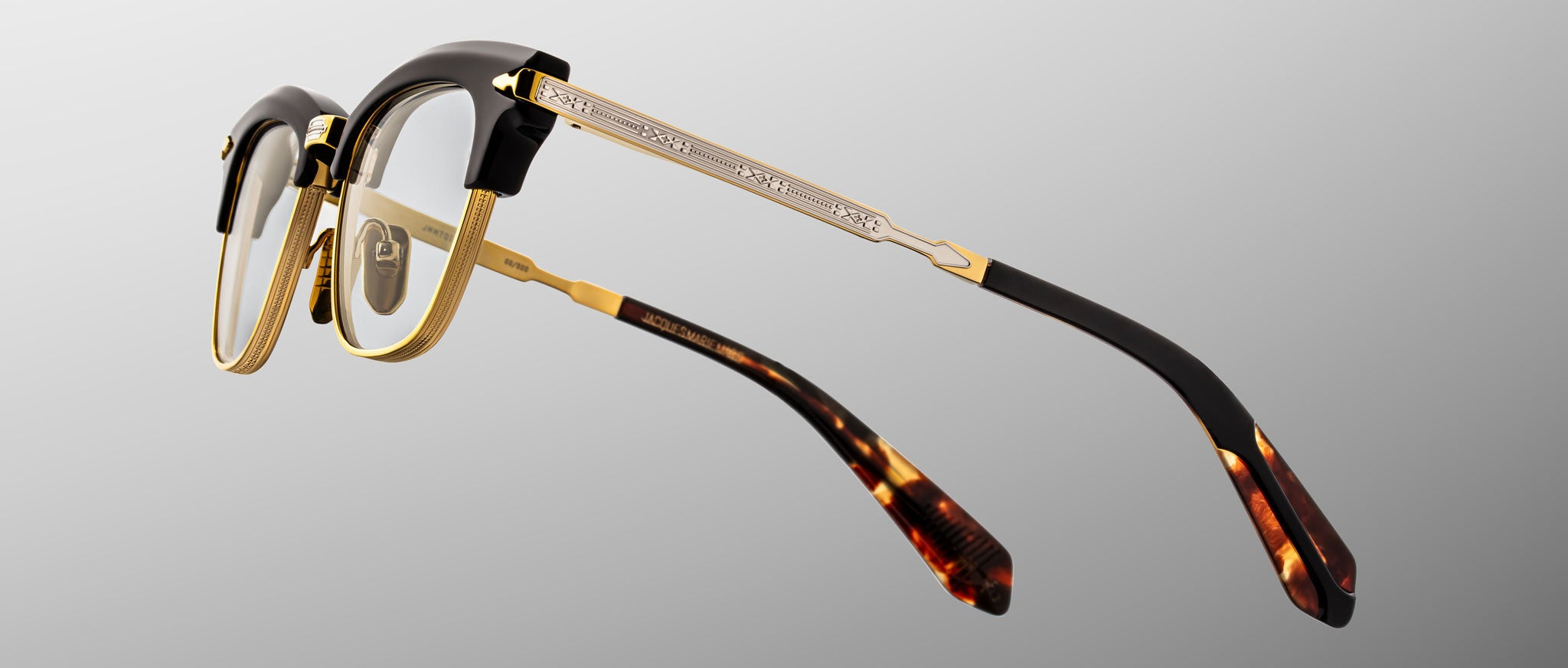The Jacques Marie Mage Sartre glasses feature gold metal frames, black accents on the browline and temples, and tortoiseshell-patterned temple tips, shown against a neutral background.