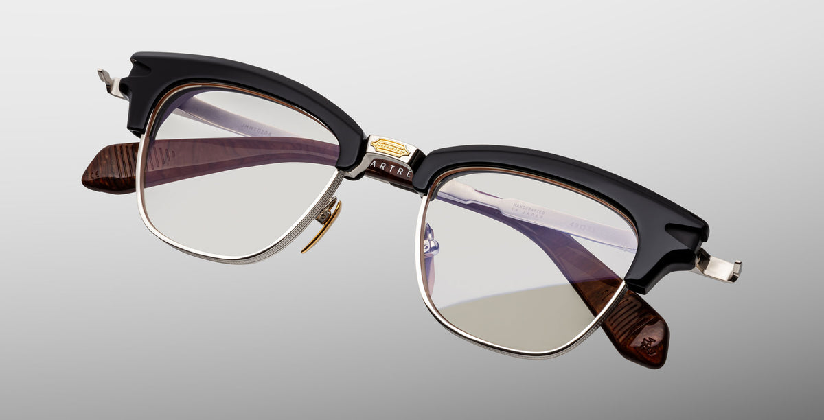 The Jacques Marie Mage Sartre by Jacques Marie Mage is a vintage-style clubmaster frame featuring black upper rims, silver metal frames, clear lenses, and brown temple arms for timeless appeal.