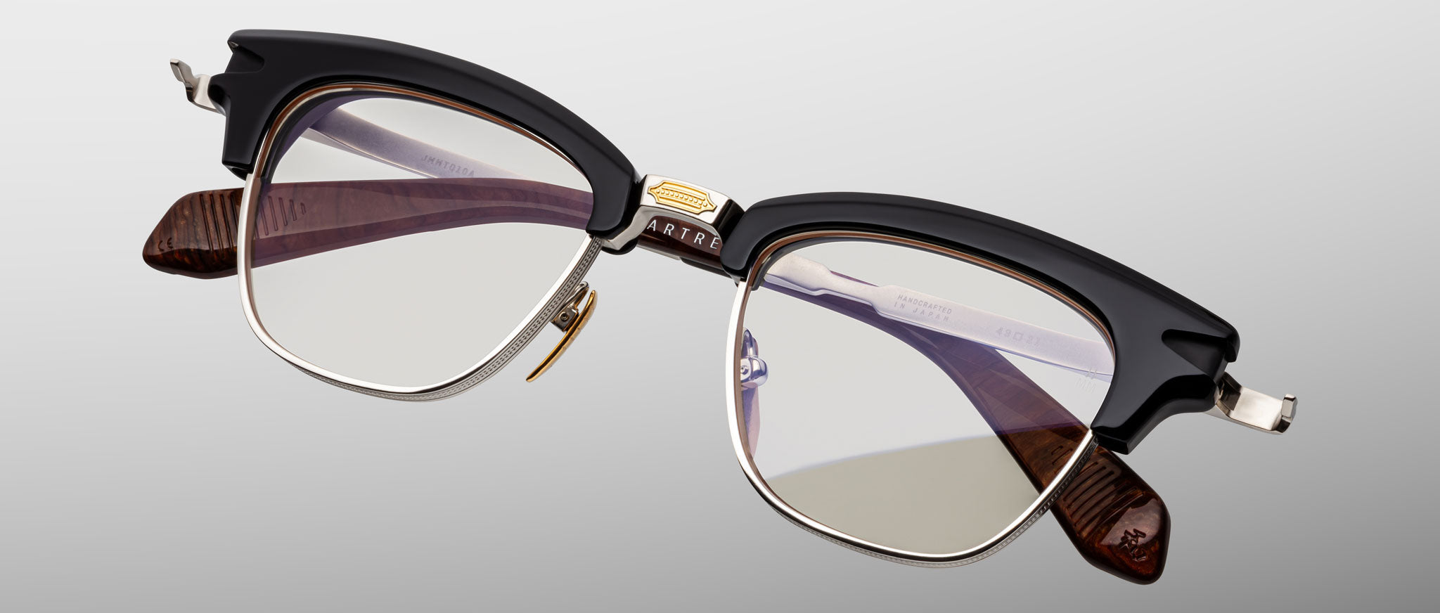 The Jacques Marie Mage Sartre by Jacques Marie Mage is a vintage-style clubmaster frame featuring black upper rims, silver metal frames, clear lenses, and brown temple arms for timeless appeal.