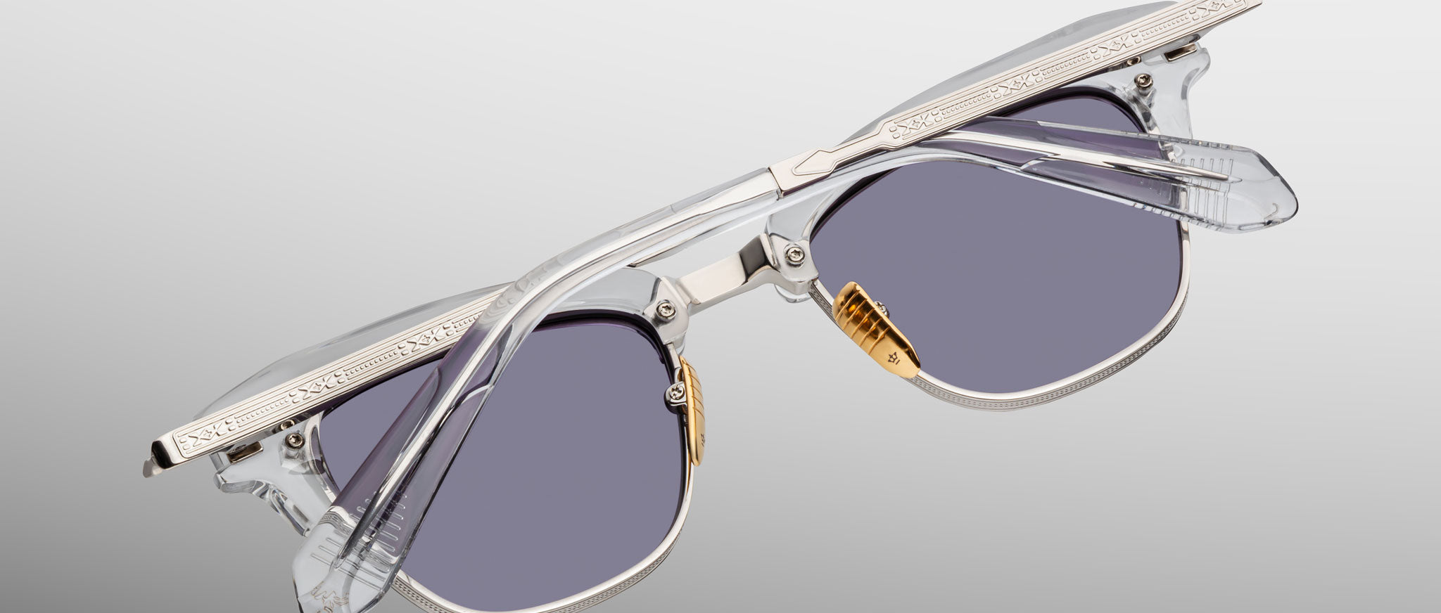 The Jacques Marie Mage Sartre glasses by Jacques Marie Mage feature clear plastic frames, silver metal accents, and gray-tinted lenses set against a plain background.