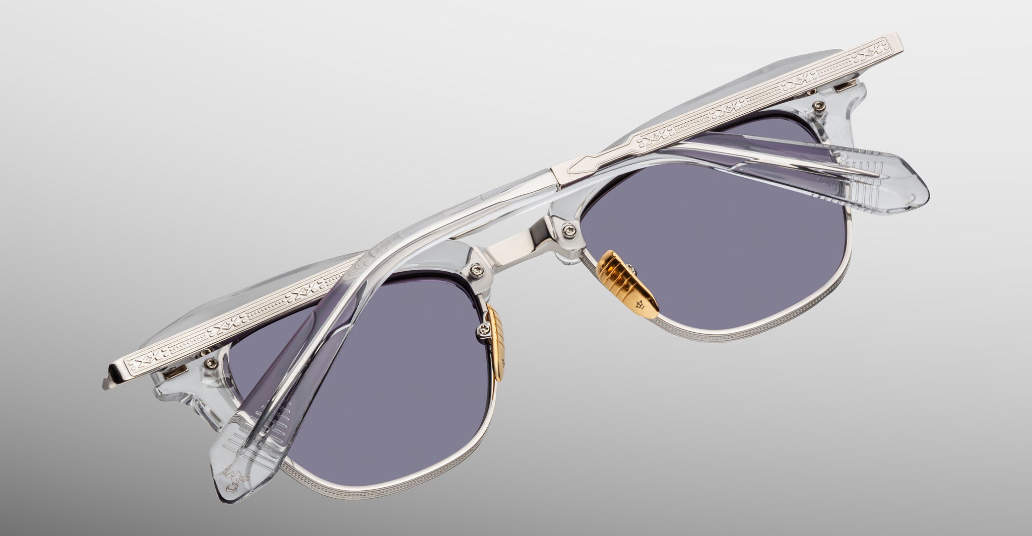 The Jacques Marie Mage Sartre glasses by Jacques Marie Mage feature clear plastic frames, silver metal accents, and gray-tinted lenses set against a plain background.