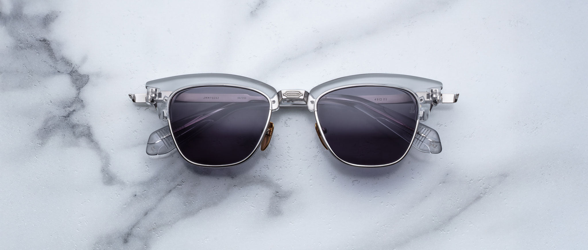 A pair of Jacques Marie Mage Sartre glasses with silver frames and dark lenses rests on a white marble surface.