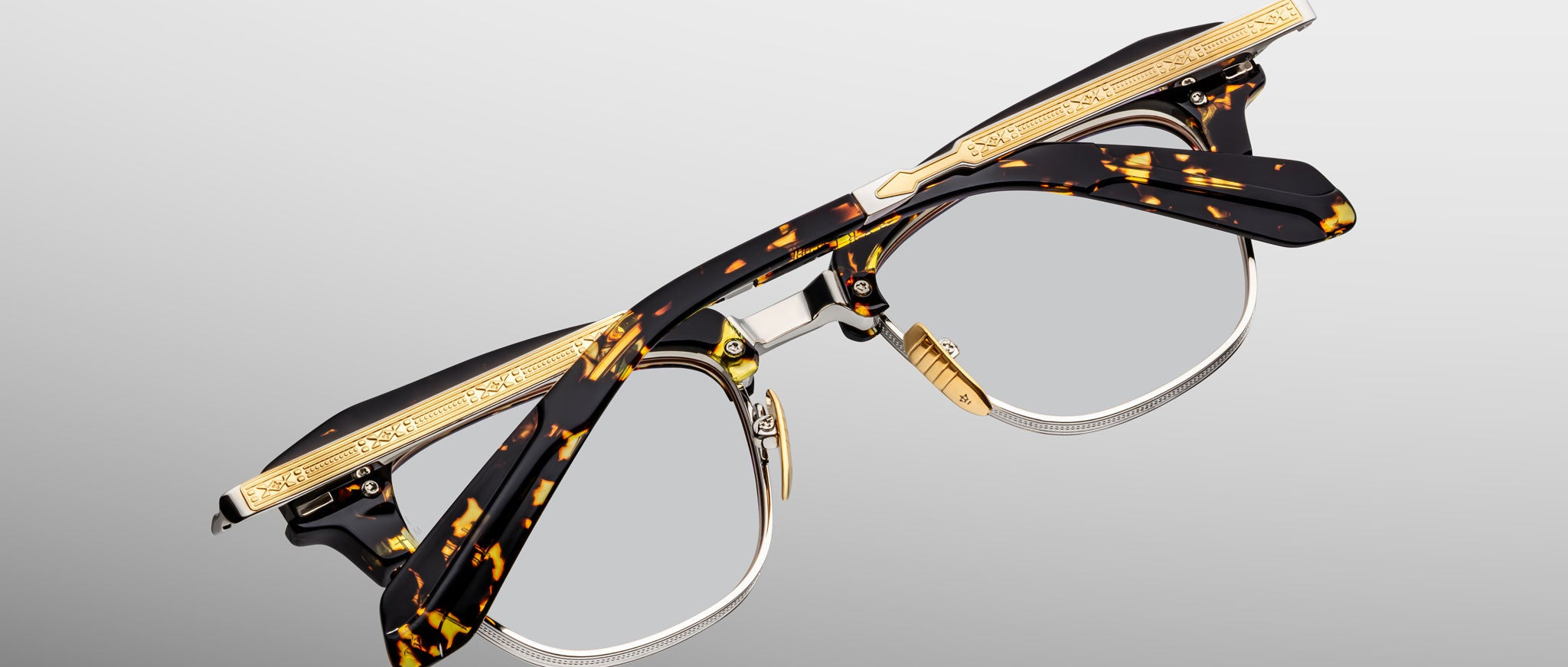 The Jacques Marie Mage Sartre glasses feature 50s-inspired clubmaster design, tortoiseshell frames, gold-tone metal accents, and engraved temple detailing, shown on a plain light background.