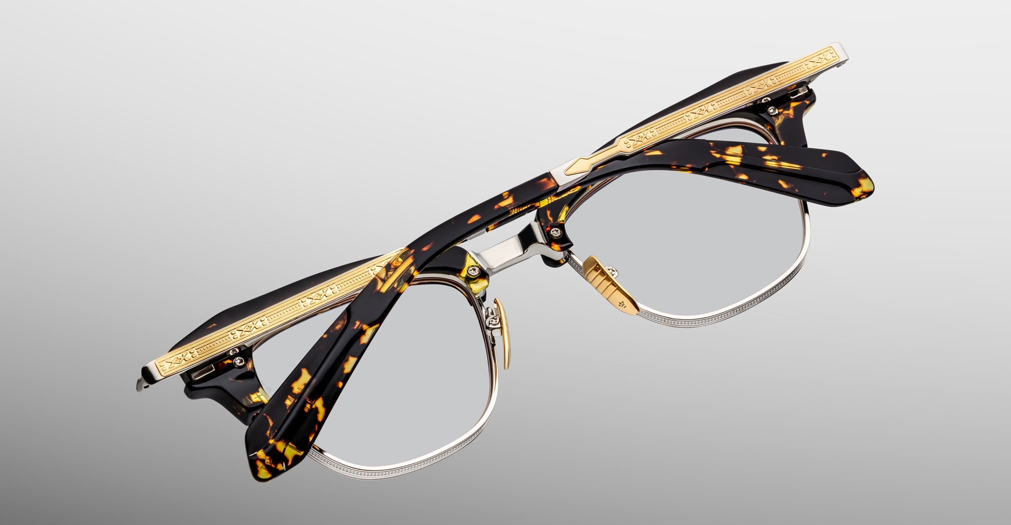 The Jacques Marie Mage Sartre glasses feature 50s-inspired clubmaster design, tortoiseshell frames, gold-tone metal accents, and engraved temple detailing, shown on a plain light background.