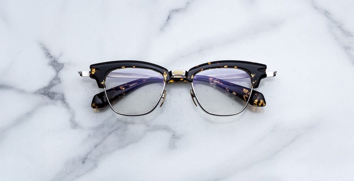 A pair of Jacques Marie Mage Sartre eyeglasses with clear lenses is displayed elegantly on a white marble surface.