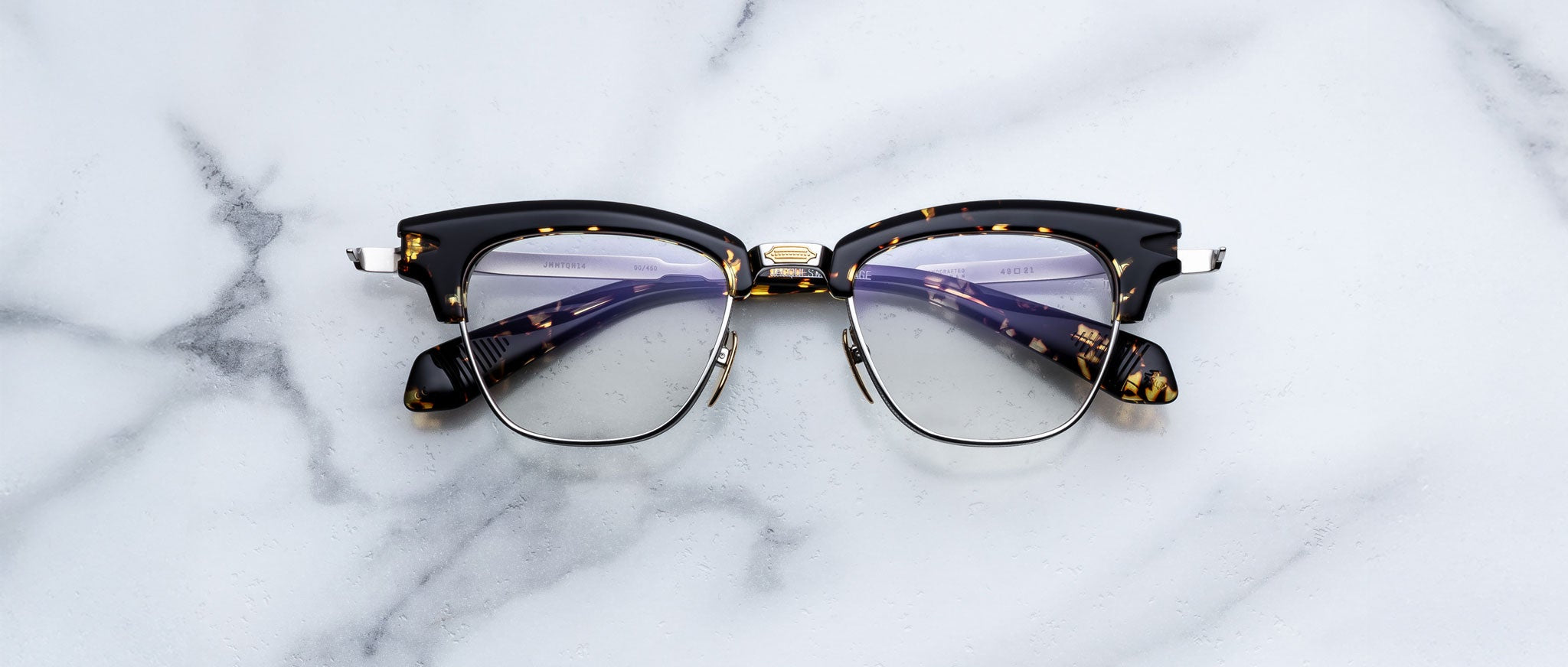 A pair of Jacques Marie Mage Sartre eyeglasses with clear lenses is displayed elegantly on a white marble surface.