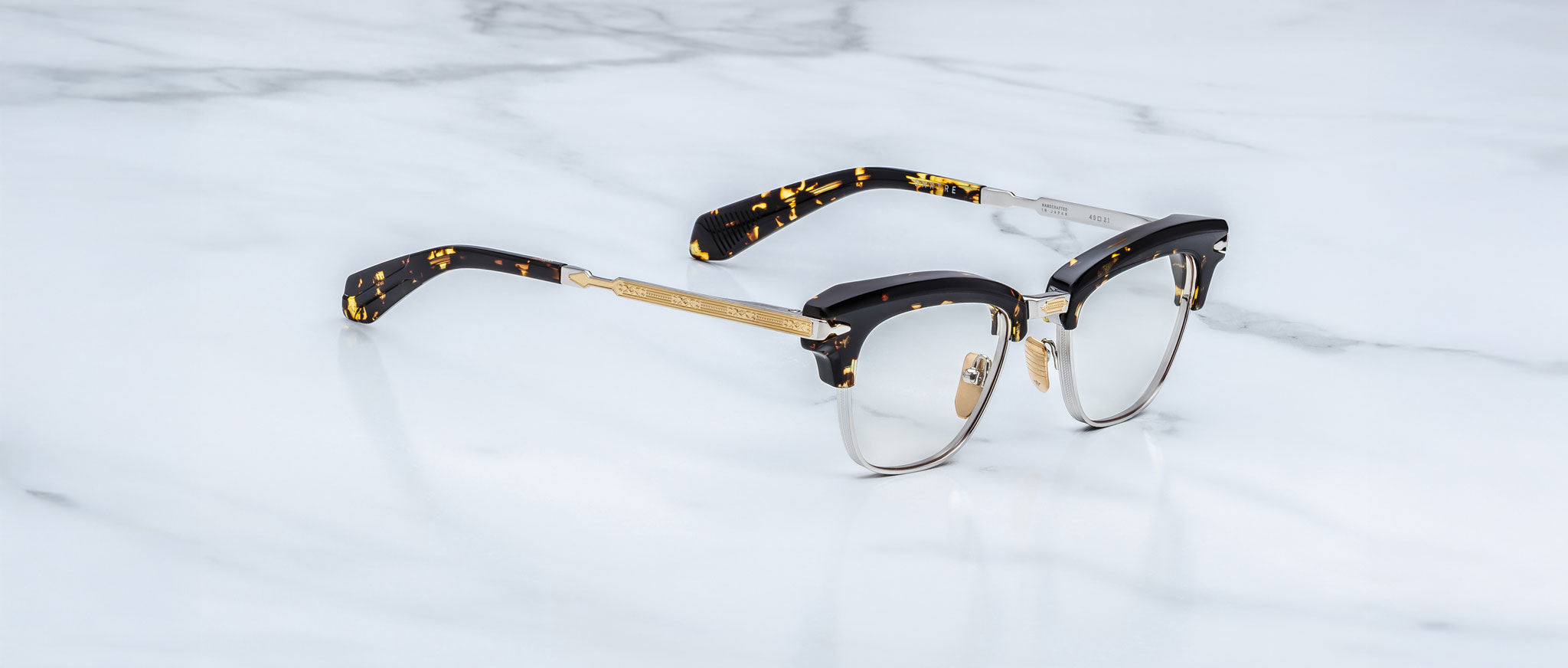Jacques Marie Mage Sartre optical eyeglasses by Jacques Marie Mage, featuring gold metal rims and black tortoiseshell arms, are displayed on a white marble surface.