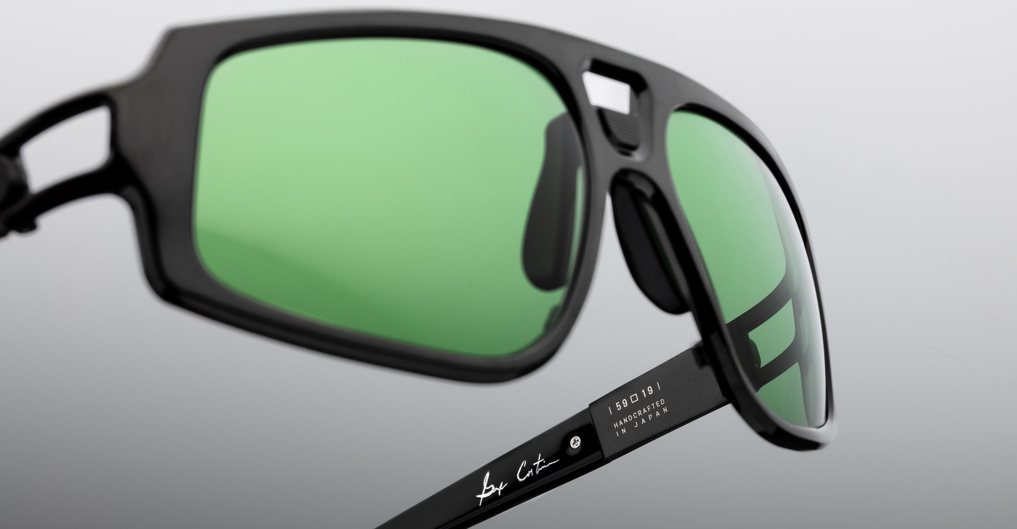 Close-up of Jacques Marie Mage Scarface black sunglasses, green polarized lenses, signature visible on the arm.