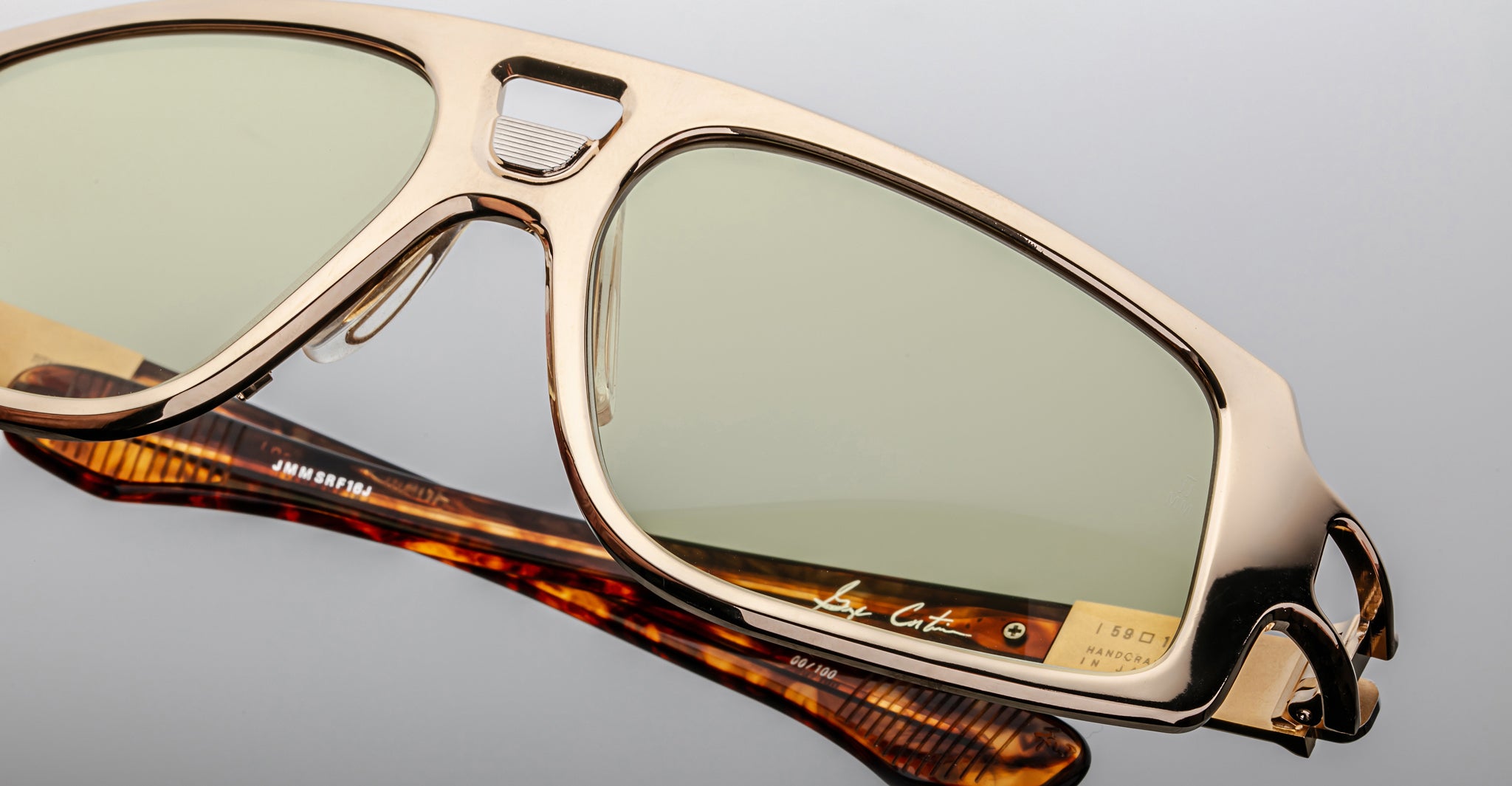 Close-up of Jacques Marie Mage Scarface sunglasses featuring gold frames, light green lenses, and tortoiseshell arms.