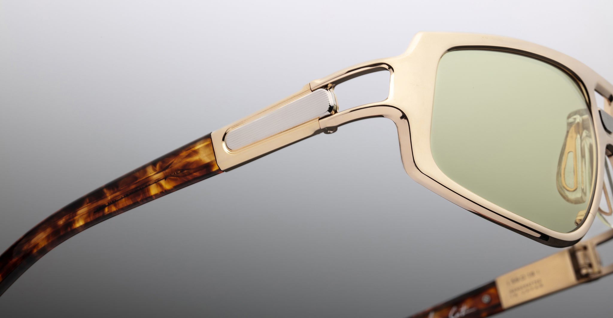 Close-up view of Jacques Marie Mage Scarface sunglasses featuring green lenses, a gold frame, and brown tortoiseshell temples.