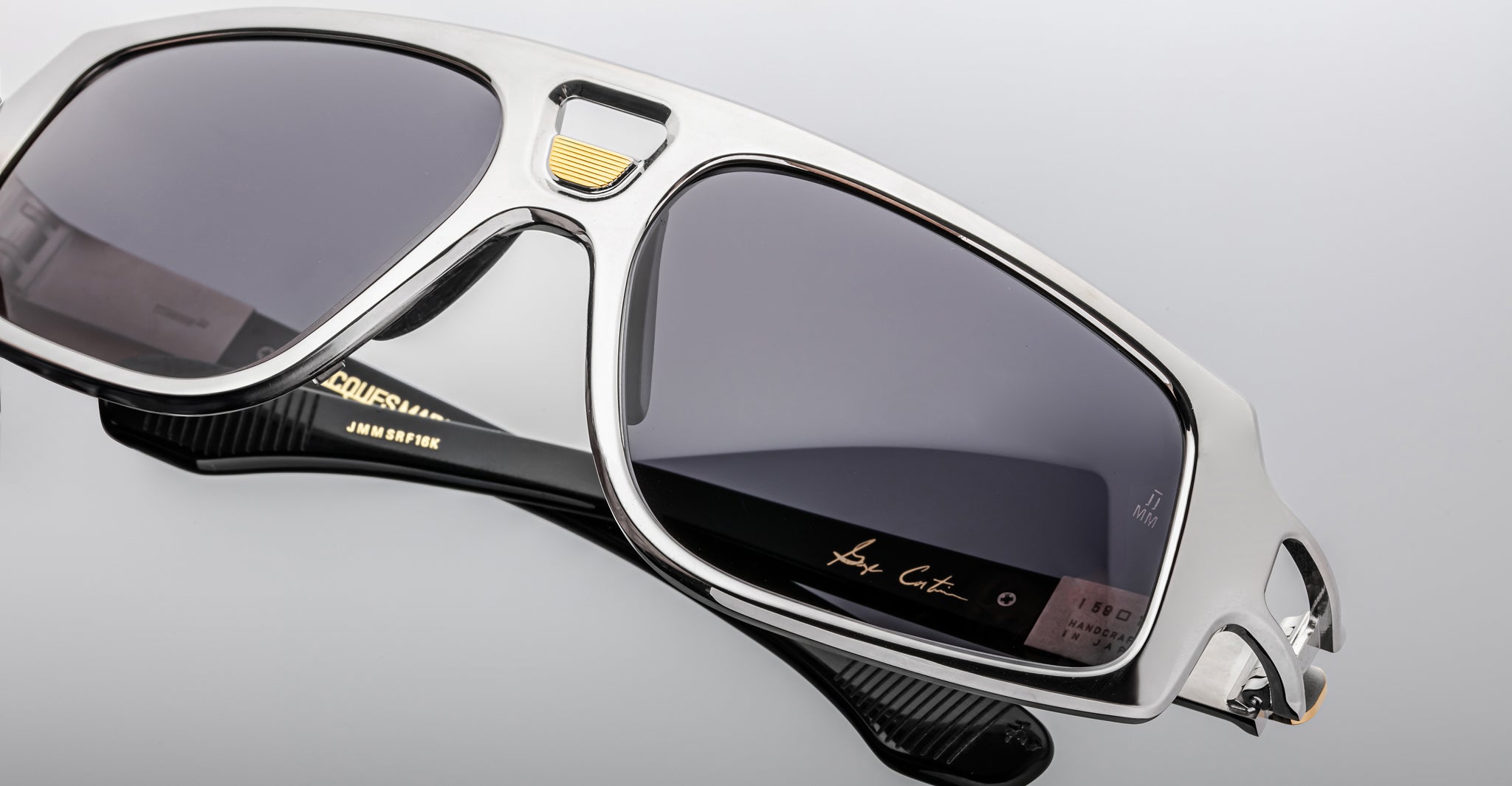Close-up of Jacques Marie Mage Scarface sunglasses with silver frame, dark lenses, and gold detailing on bridge and temples.