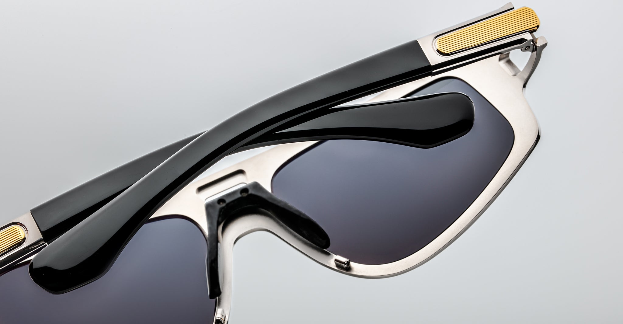 Close-up of folded Jacques Marie Mage Scarface sunglasses in black and silver with gold accents, viewed from the side.