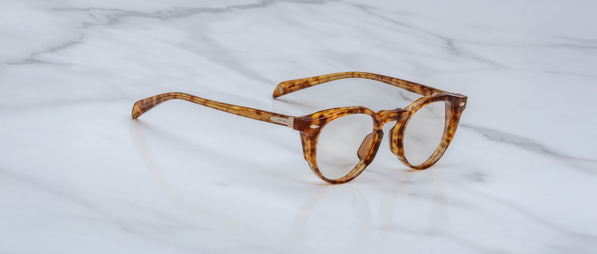 The Jacques Marie Mage Sheridan, round tortoiseshell eyeglasses with thick frames, rest on a white marble surface.