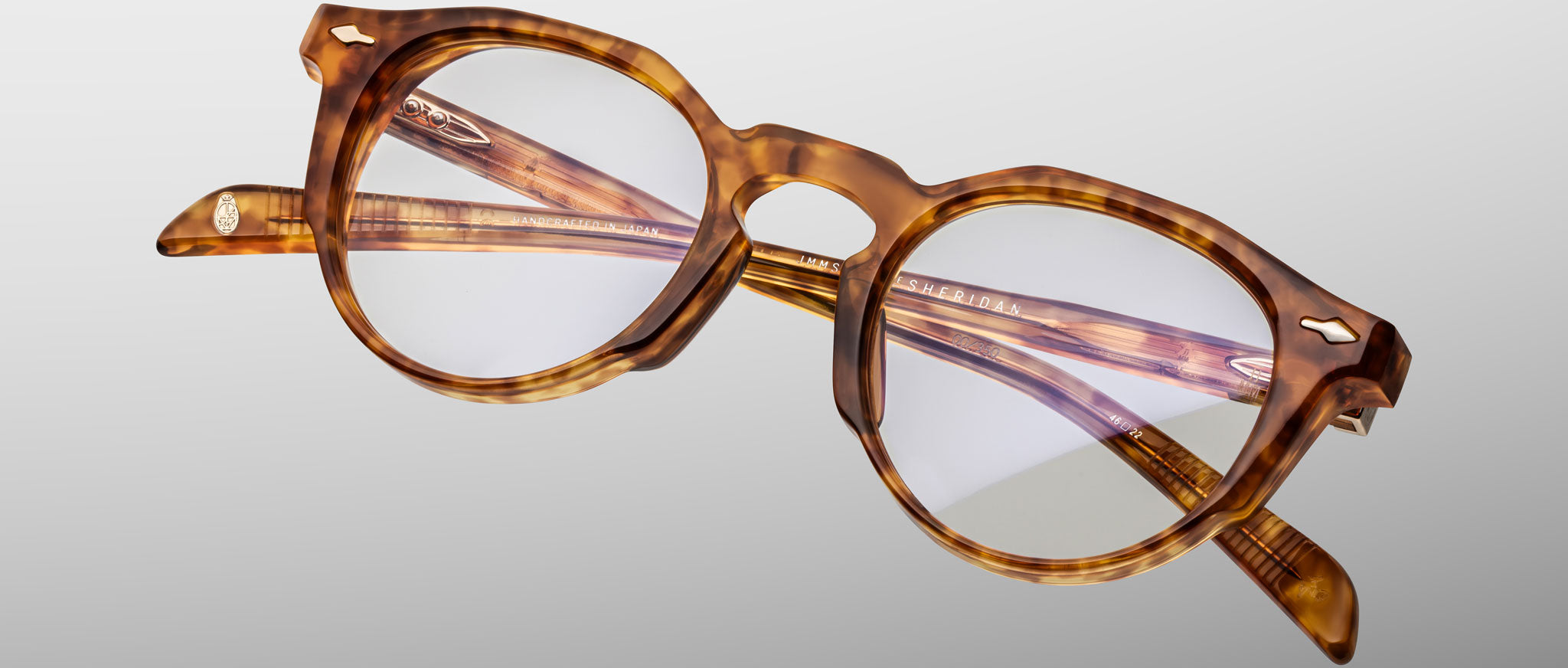 The Jacques Marie Mage Sheridan eyeglasses feature round, thick tortoiseshell frames with clear lenses, displayed against a plain light gray background.