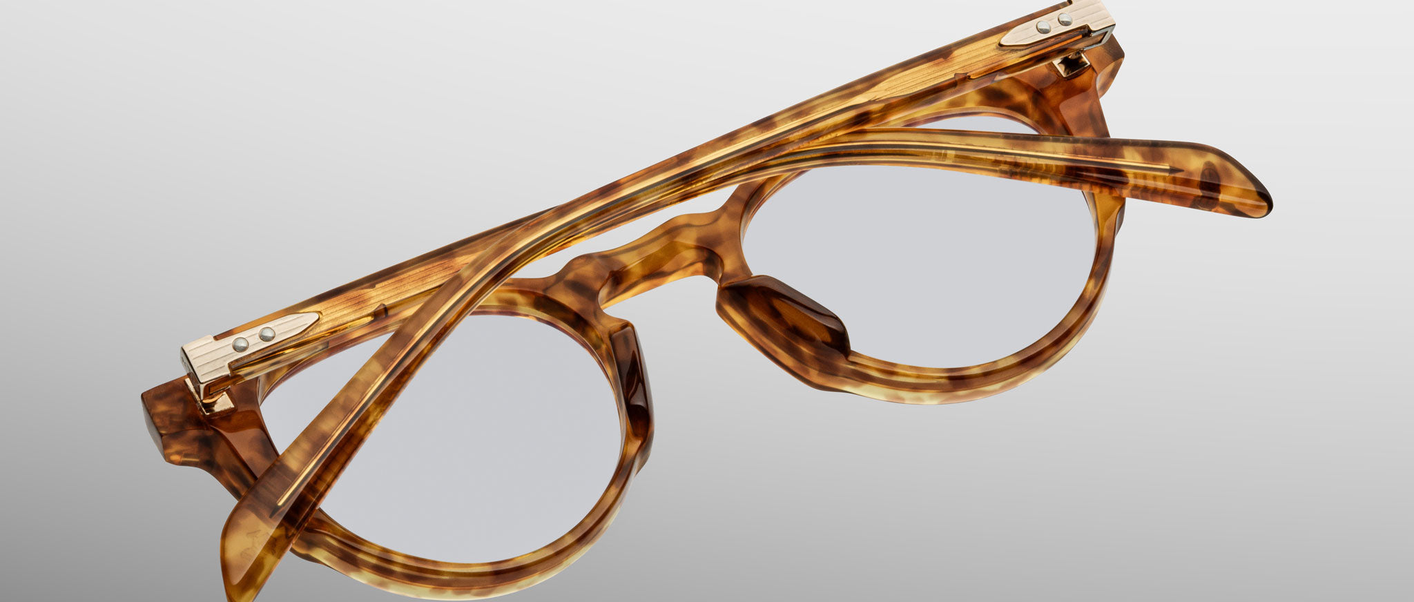 The Jacques Marie Mage Sheridan eyeglasses, featuring a round tortoiseshell-patterned frame with metal hinge accents on the temples and folded arms, are displayed on a light gray background.