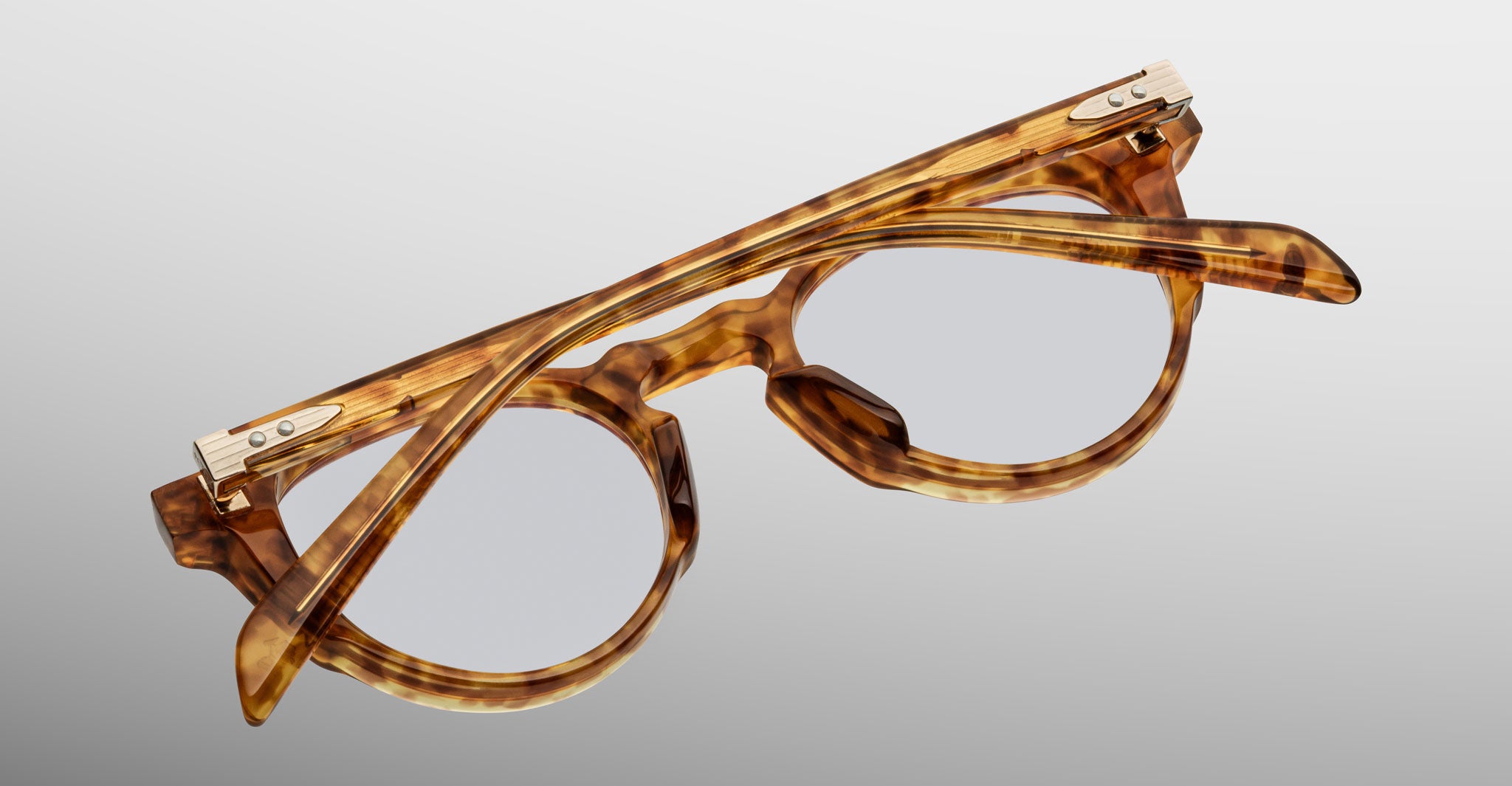 The Jacques Marie Mage Sheridan eyeglasses, featuring a round tortoiseshell-patterned frame with metal hinge accents on the temples and folded arms, are displayed on a light gray background.
