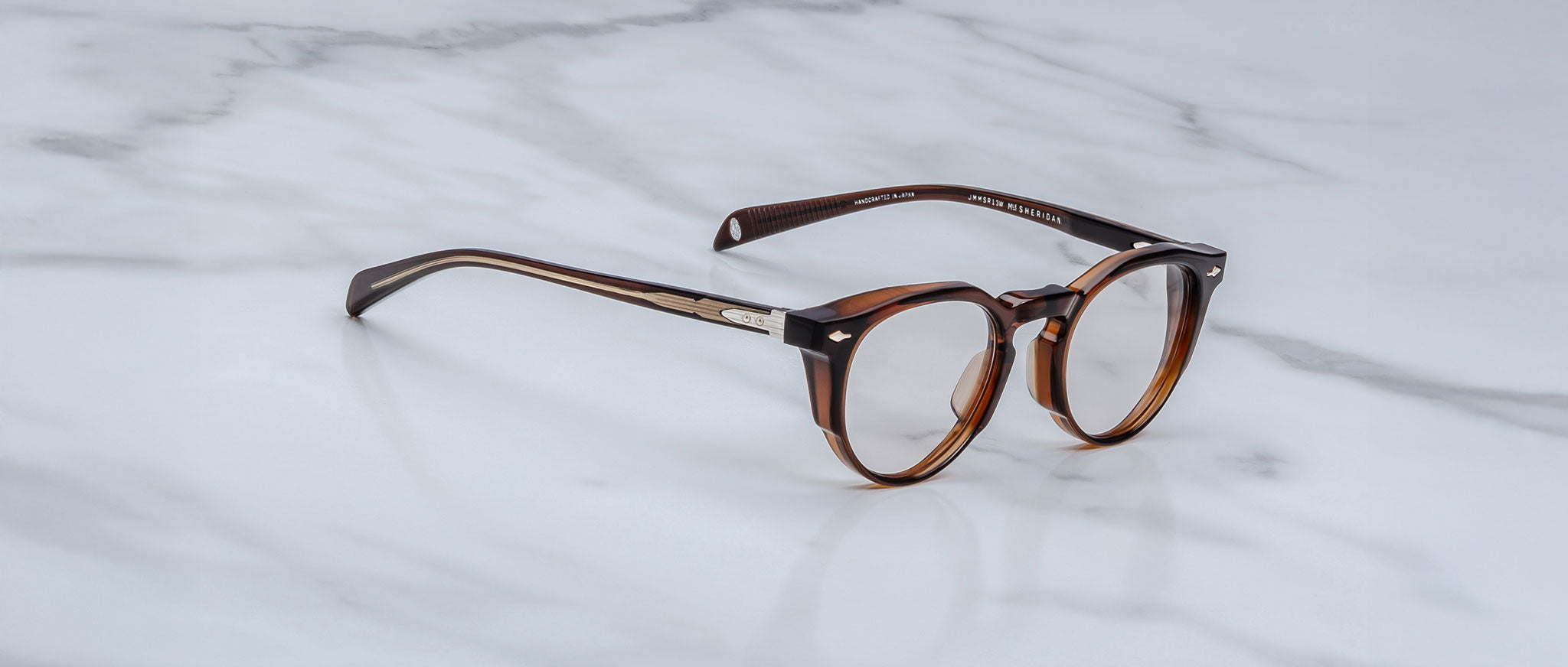 The Jacques Marie Mage Sheridan are round, brown tortoiseshell eyeglasses with silver temple accents, displayed on a white marble surface.
