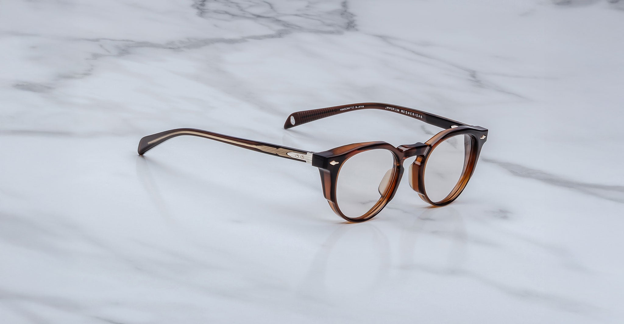 The Jacques Marie Mage Sheridan are round, brown tortoiseshell eyeglasses with silver temple accents, displayed on a white marble surface.