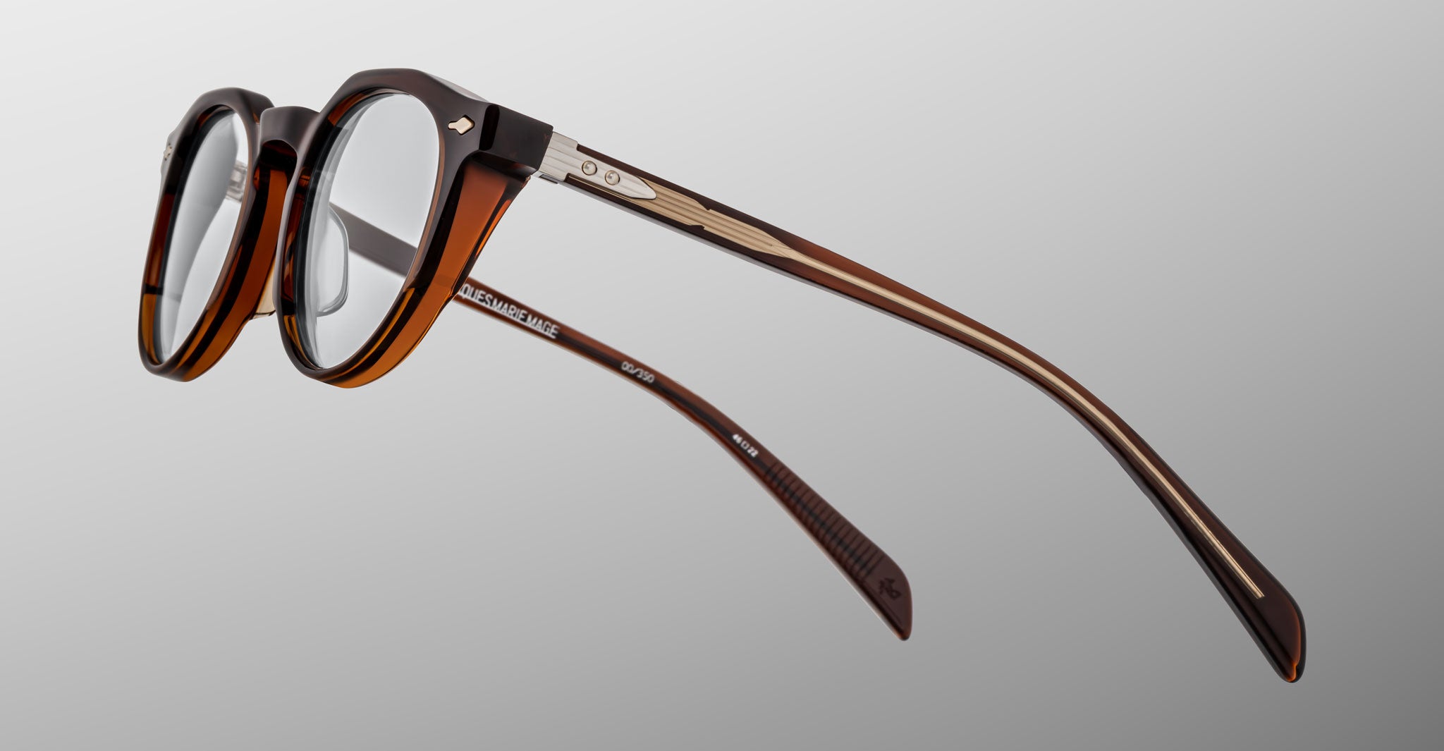 Jacques Marie Mage Sheridan: brown, semi-transparent round eyeglasses with metal temple accents, shown at an angle on a plain gray background.