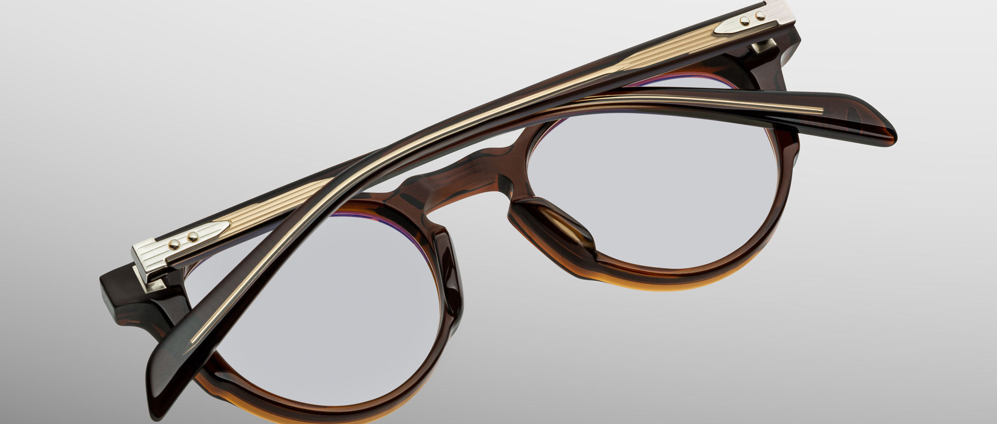 The Jacques Marie Mage Sheridan eyeglasses, round and brown in acetate with metal hinges, are shown folded lens-side down on a light gray background.