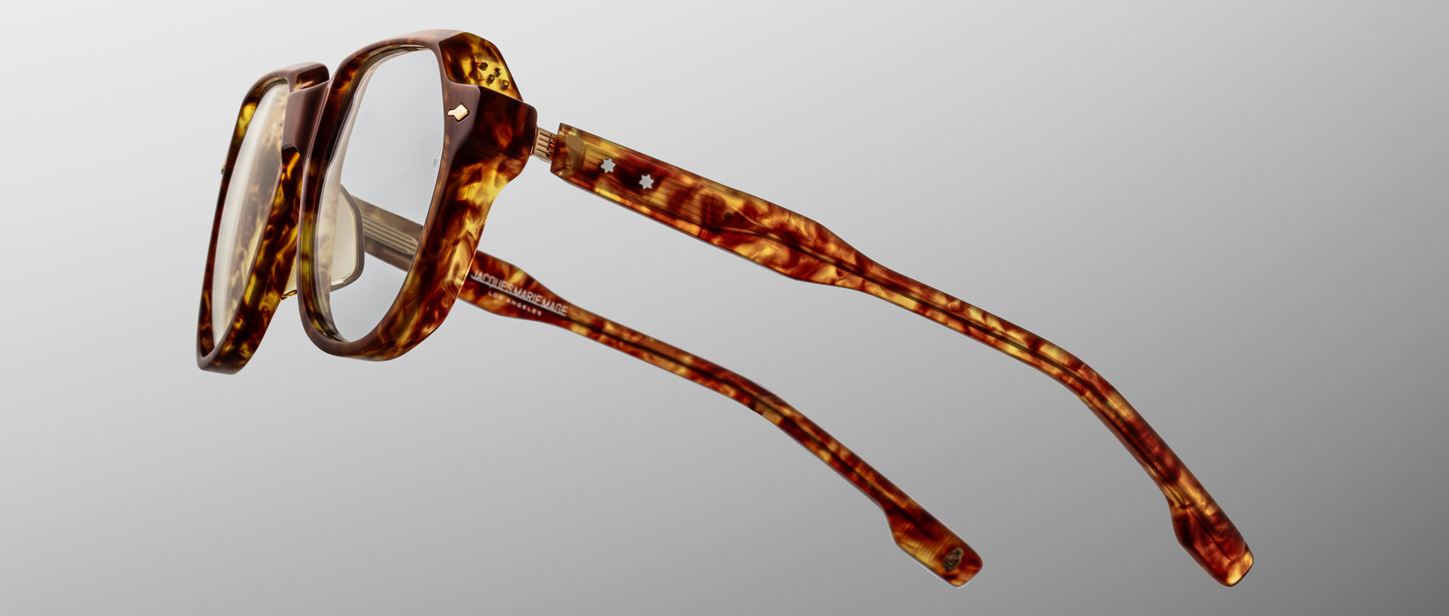 The Jacques Marie Mage Shozo eyeglasses feature thick, rectangular brown tortoiseshell frames with gently curved arms, shown against a light gray gradient background.